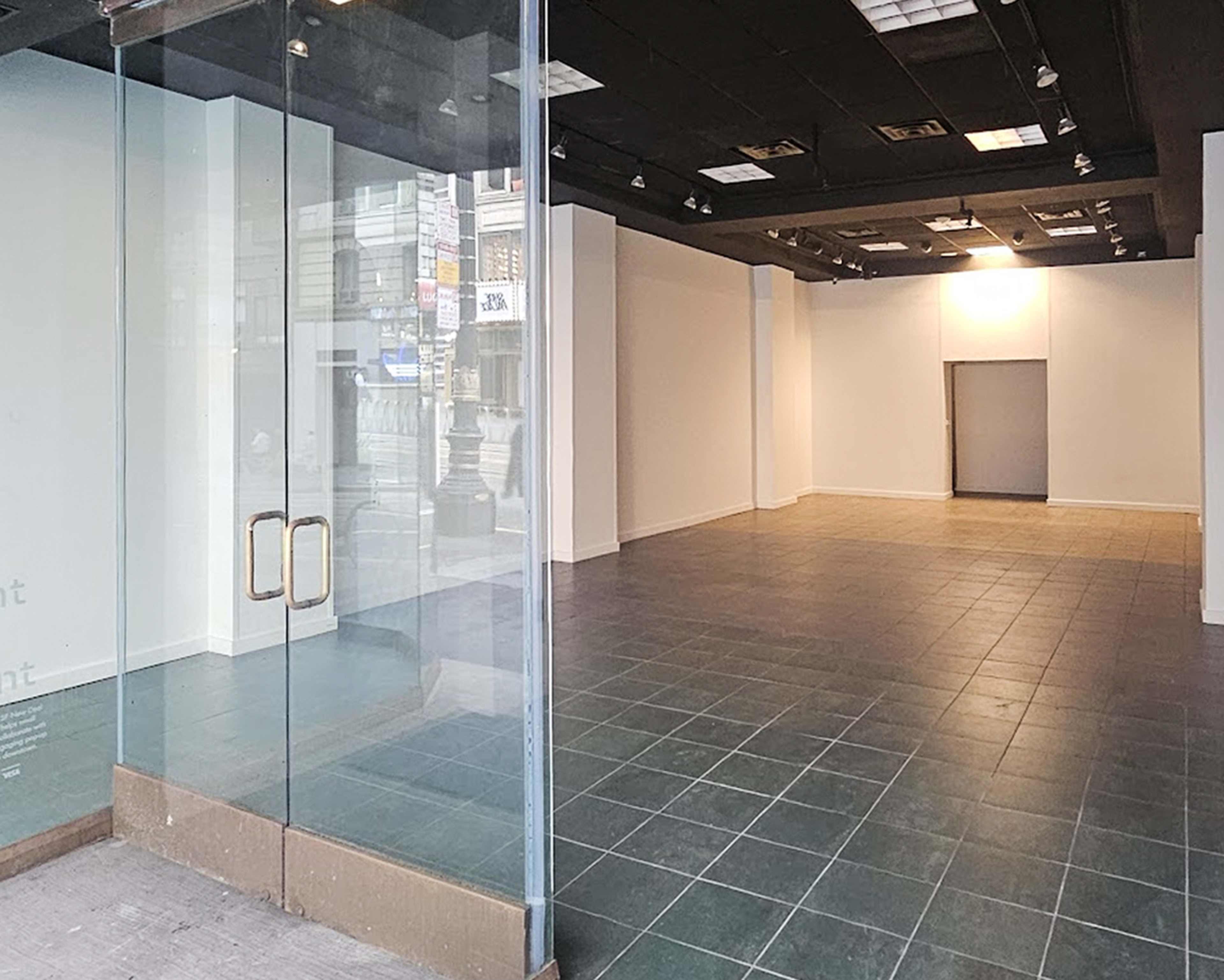 The image shows an empty retail space with glass doors, tiled flooring, and a single doorway at the far end.