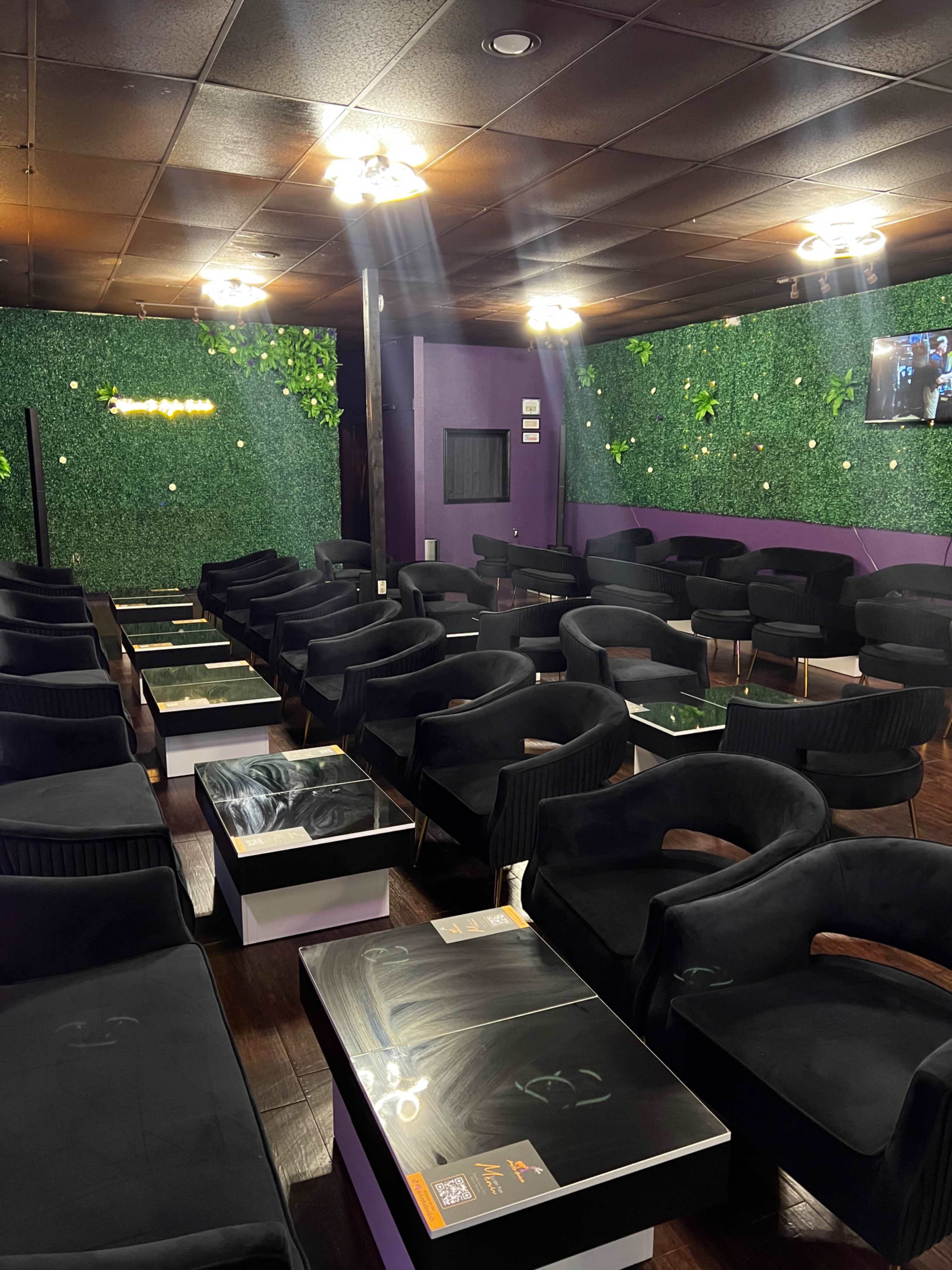 An interior space with multiple black chairs arranged around low tables, set against a wall covered in green foliage.