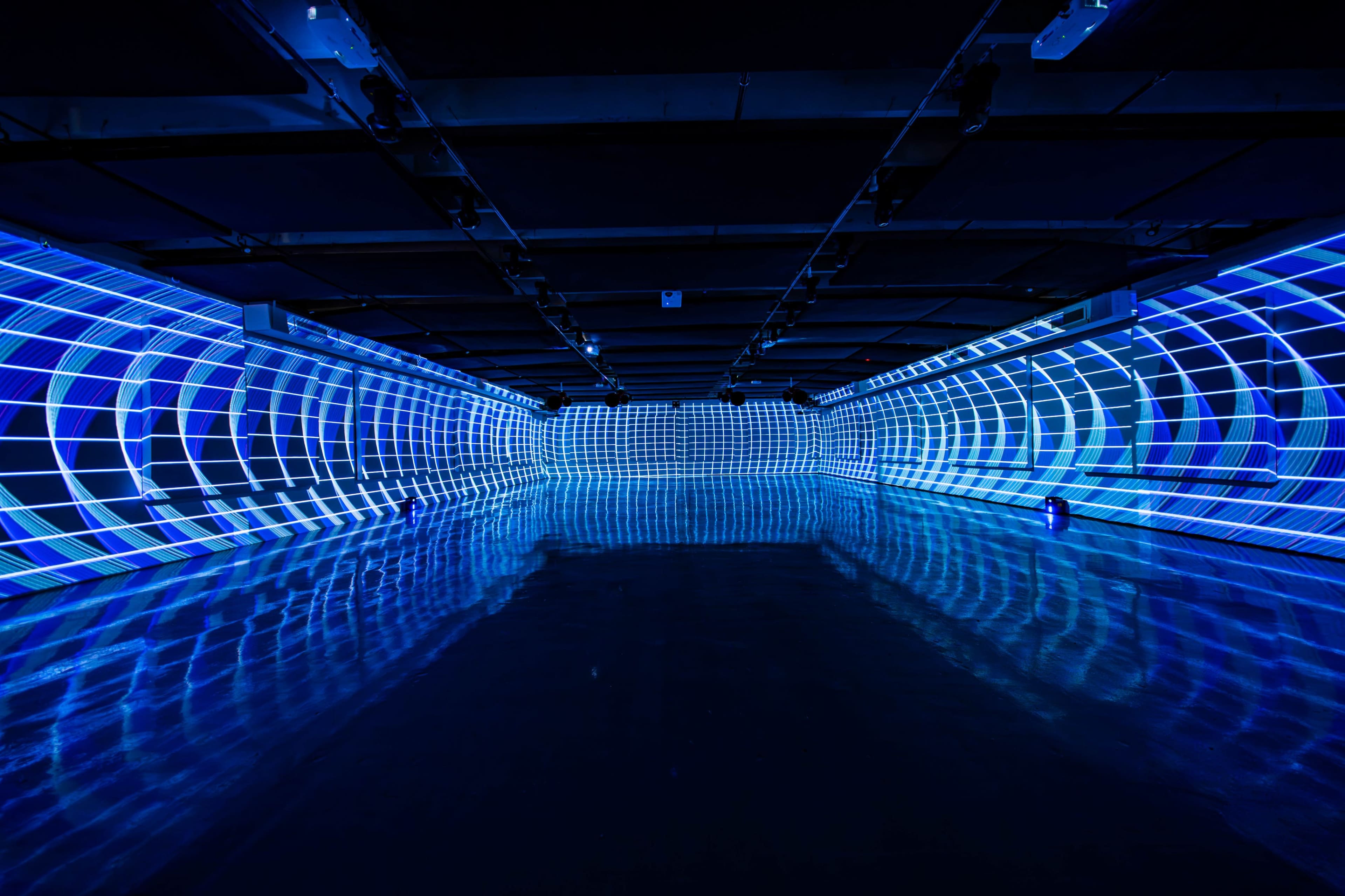 The image shows a large, illuminated space with blue light projections creating a grid pattern on the walls and floor.