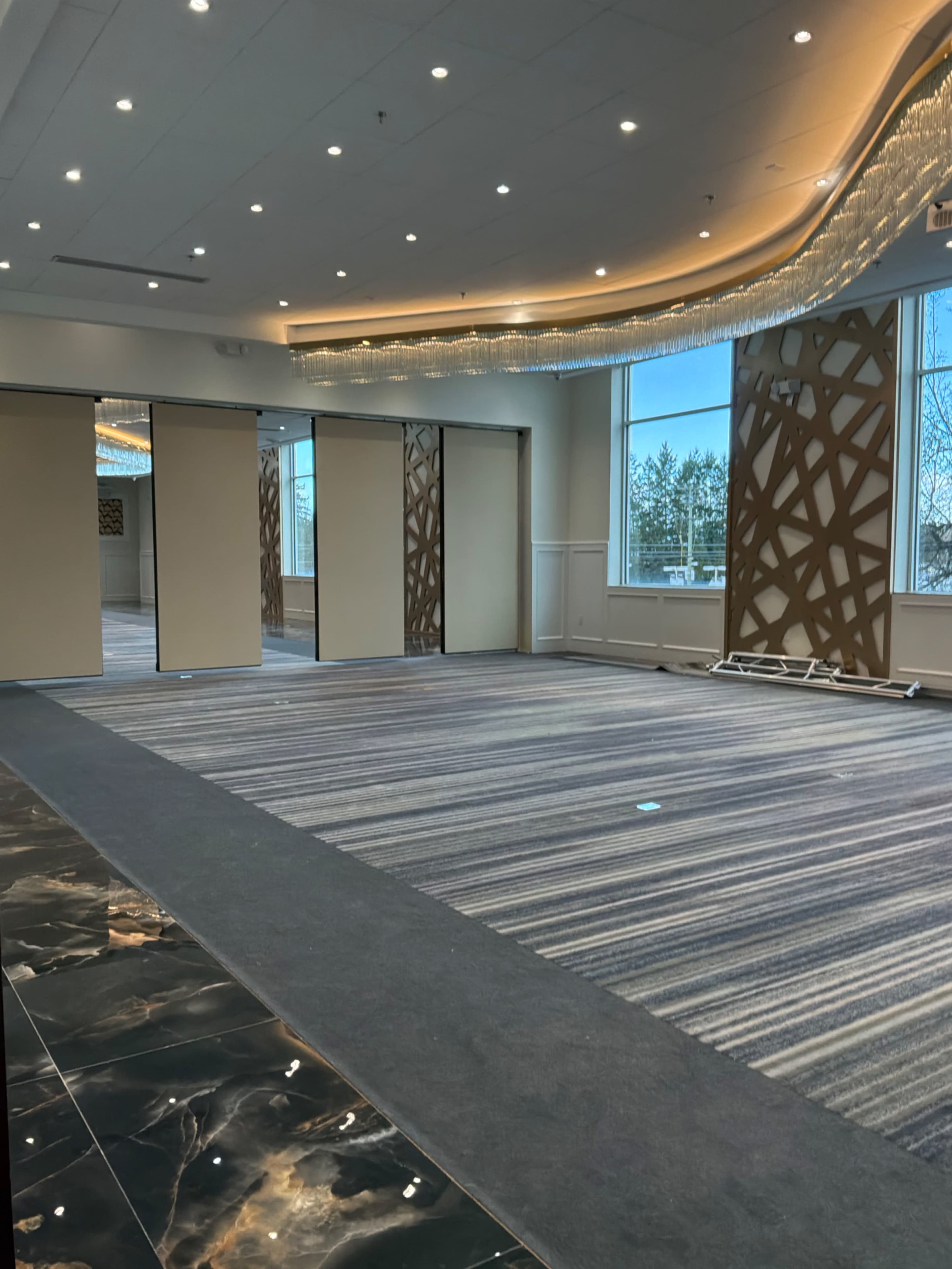 The image shows a spacious indoor venue with a carpeted floor, decorative wall panels, and large sliding doors that open to natural light.