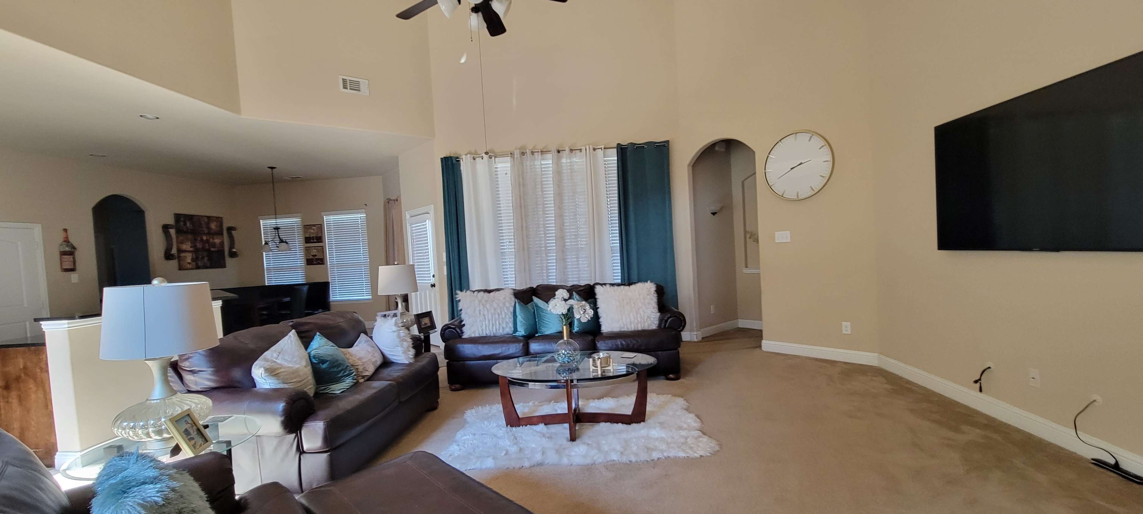 The living room features two leather sofas, a glass coffee table on a rug, and large windows with blue curtains.
