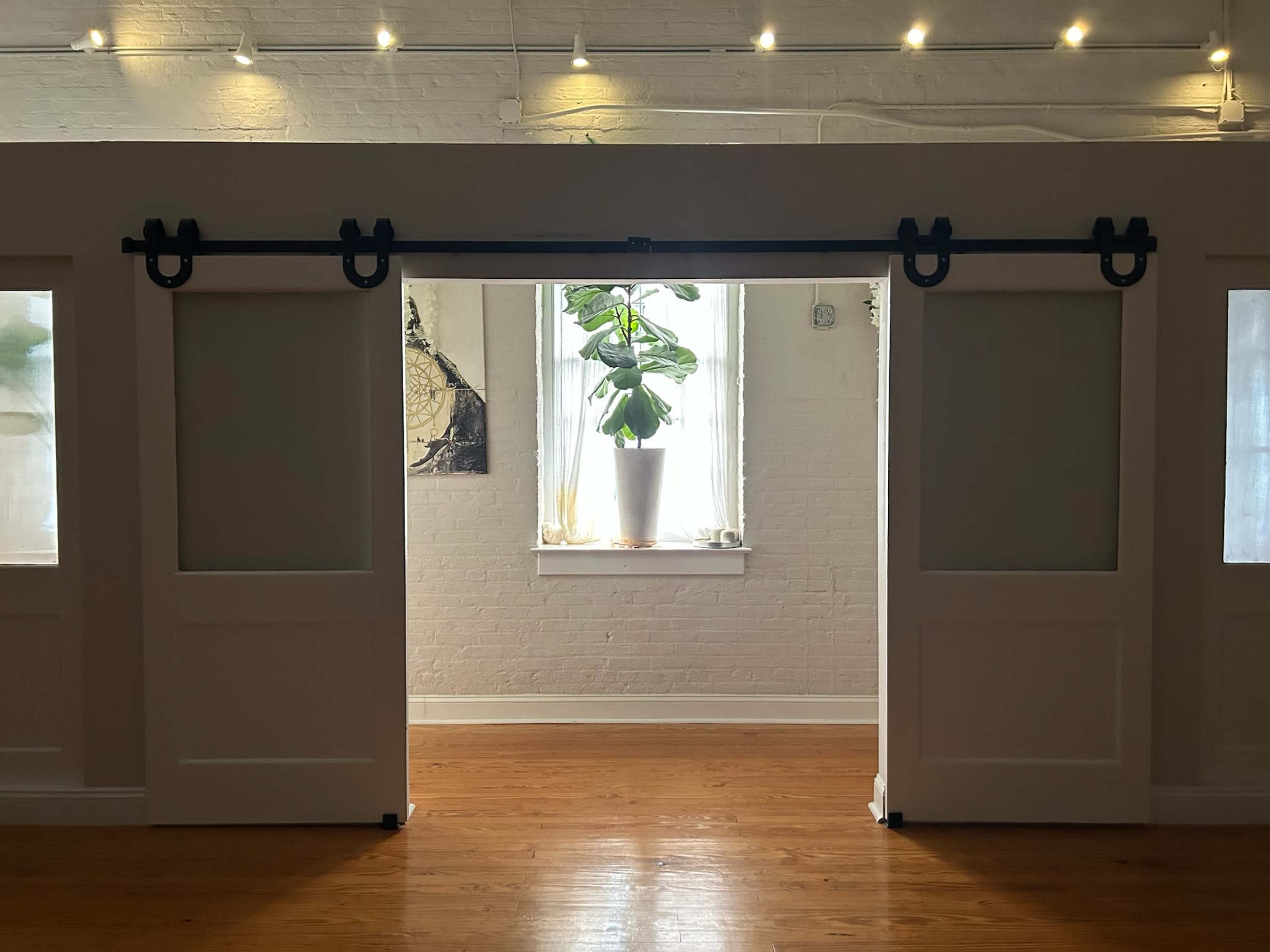 The image shows a well-lit interior space with sliding barn doors and a window featuring a potted plant.