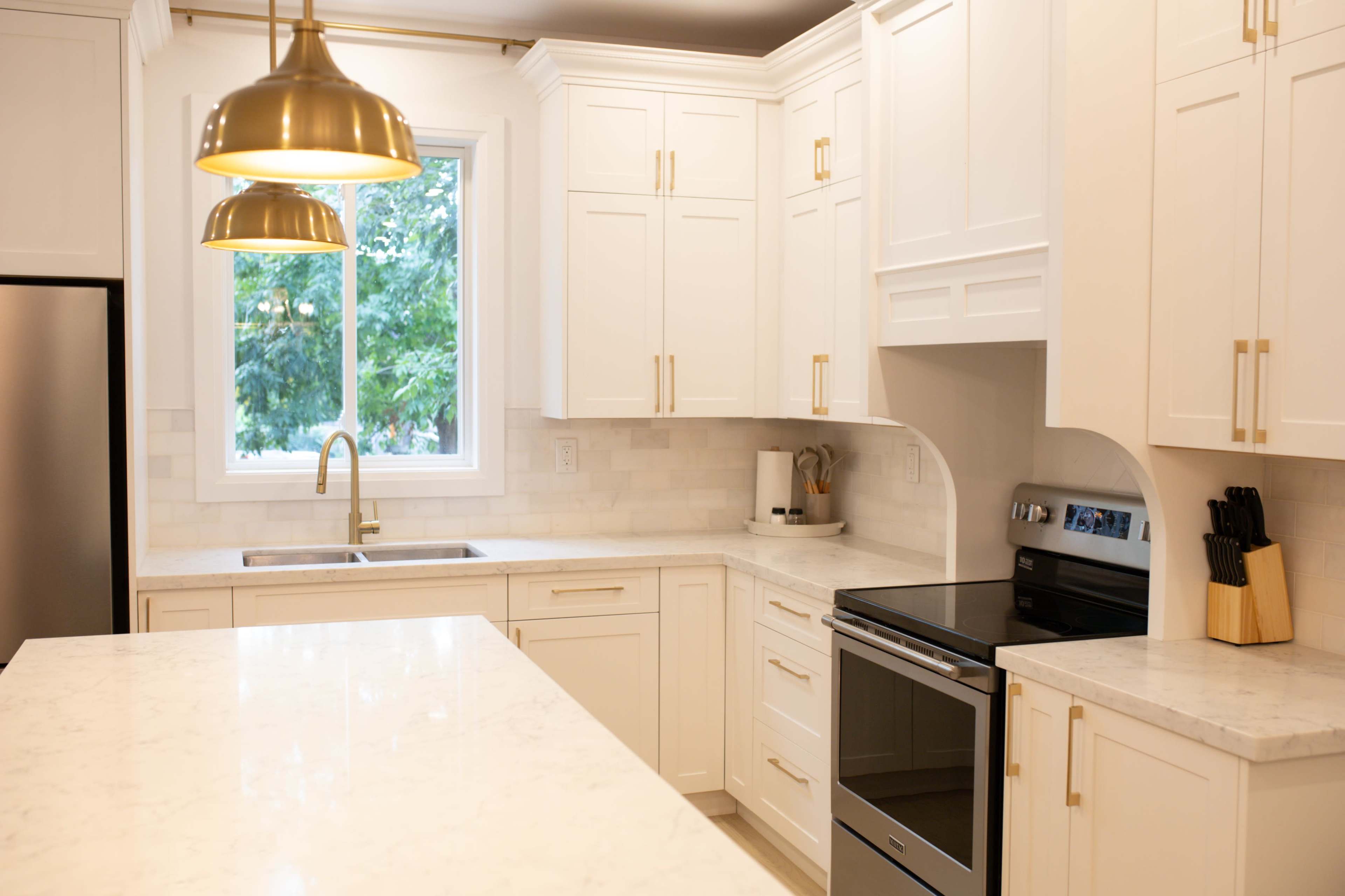 A modern kitchen features white cabinets, a large marble countertop, a stainless steel oven, and a window that allows natural light to enter.