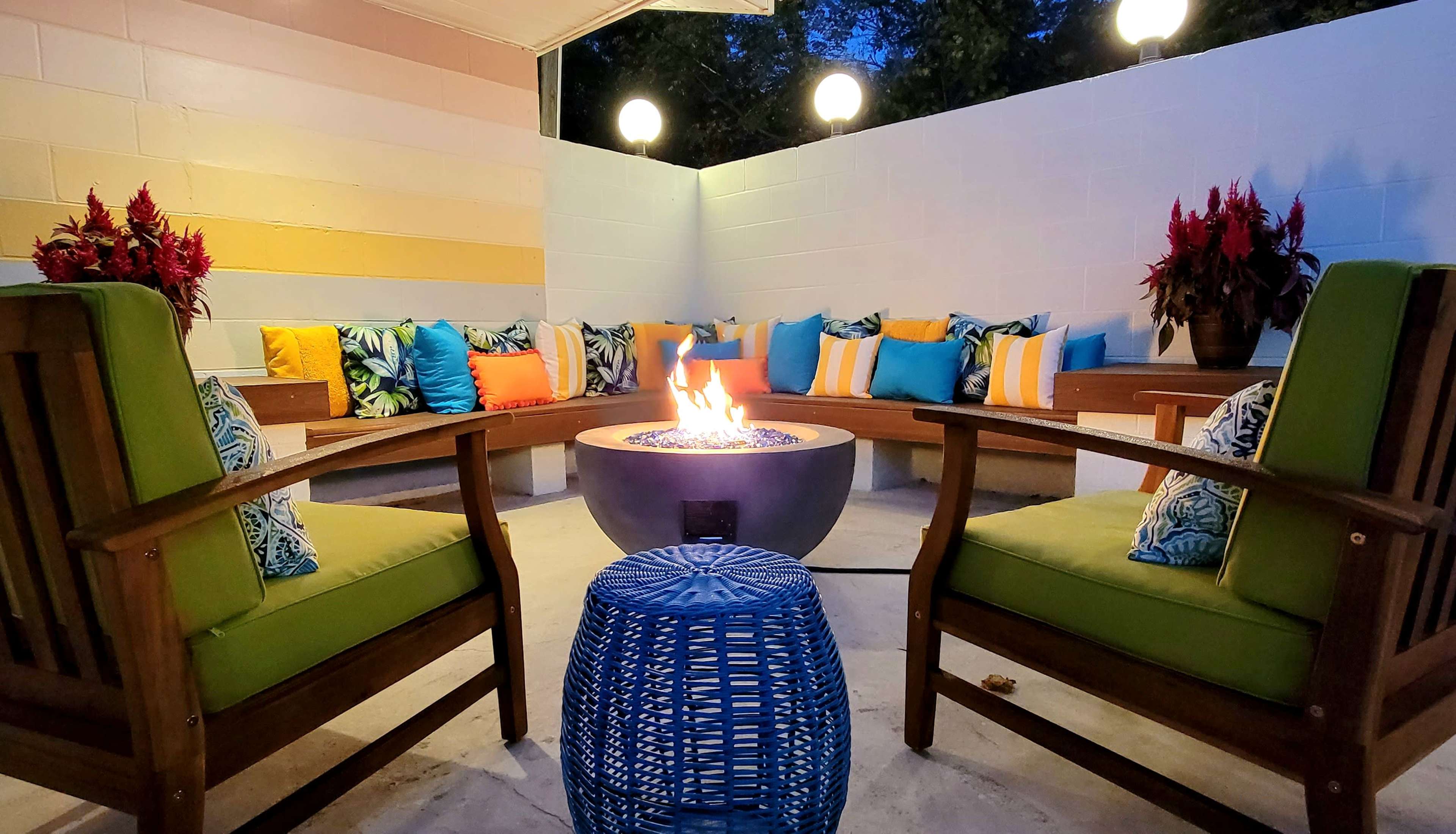 A cozy outdoor seating area features circular seating around a fire pit, with brightly colored cushions and decorative plants.