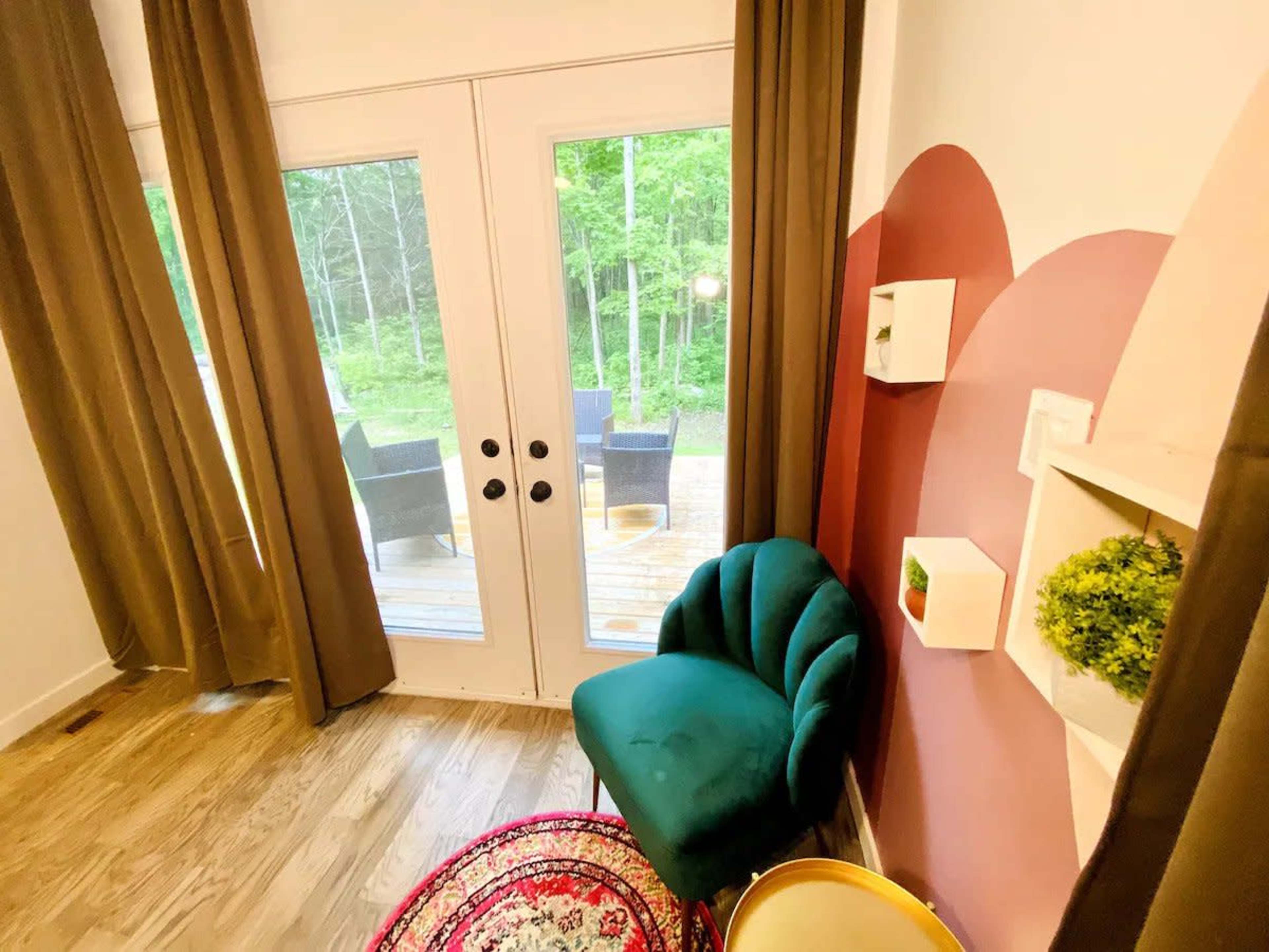 A small interior corner with a green chair, a patterned rug, and large glass doors leading to a deck with outdoor seating.