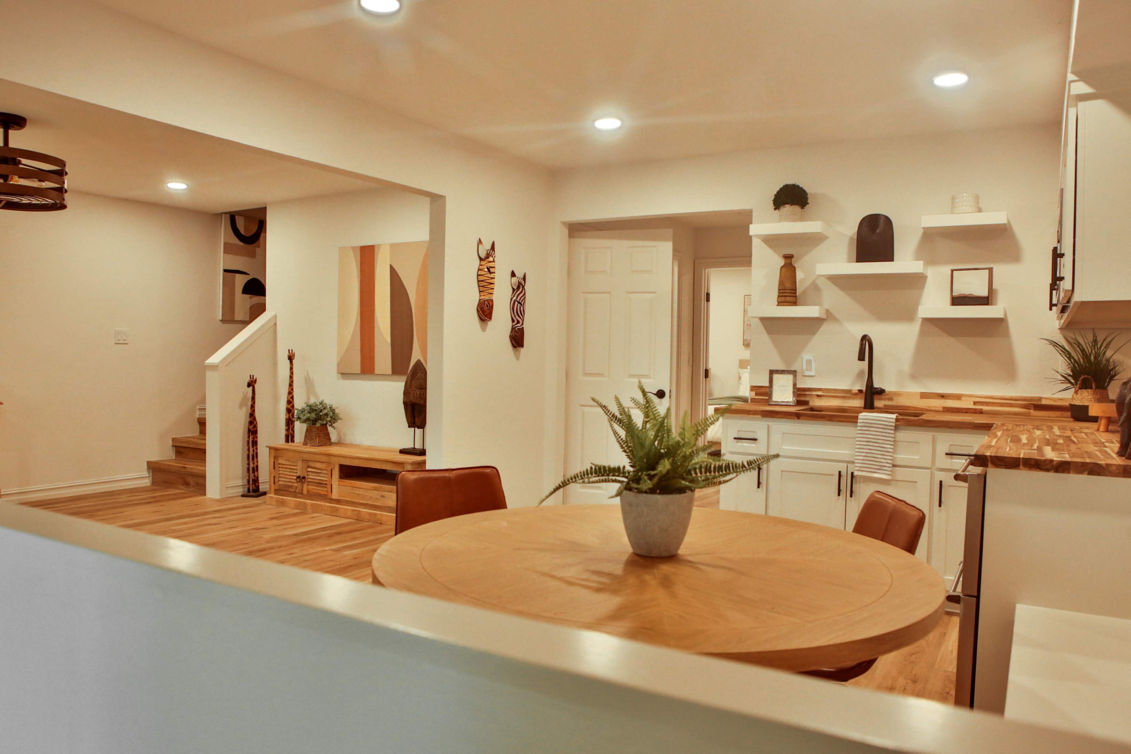 A modern kitchen and dining area featuring a round wooden table, white cabinetry, and decorative elements on the walls.