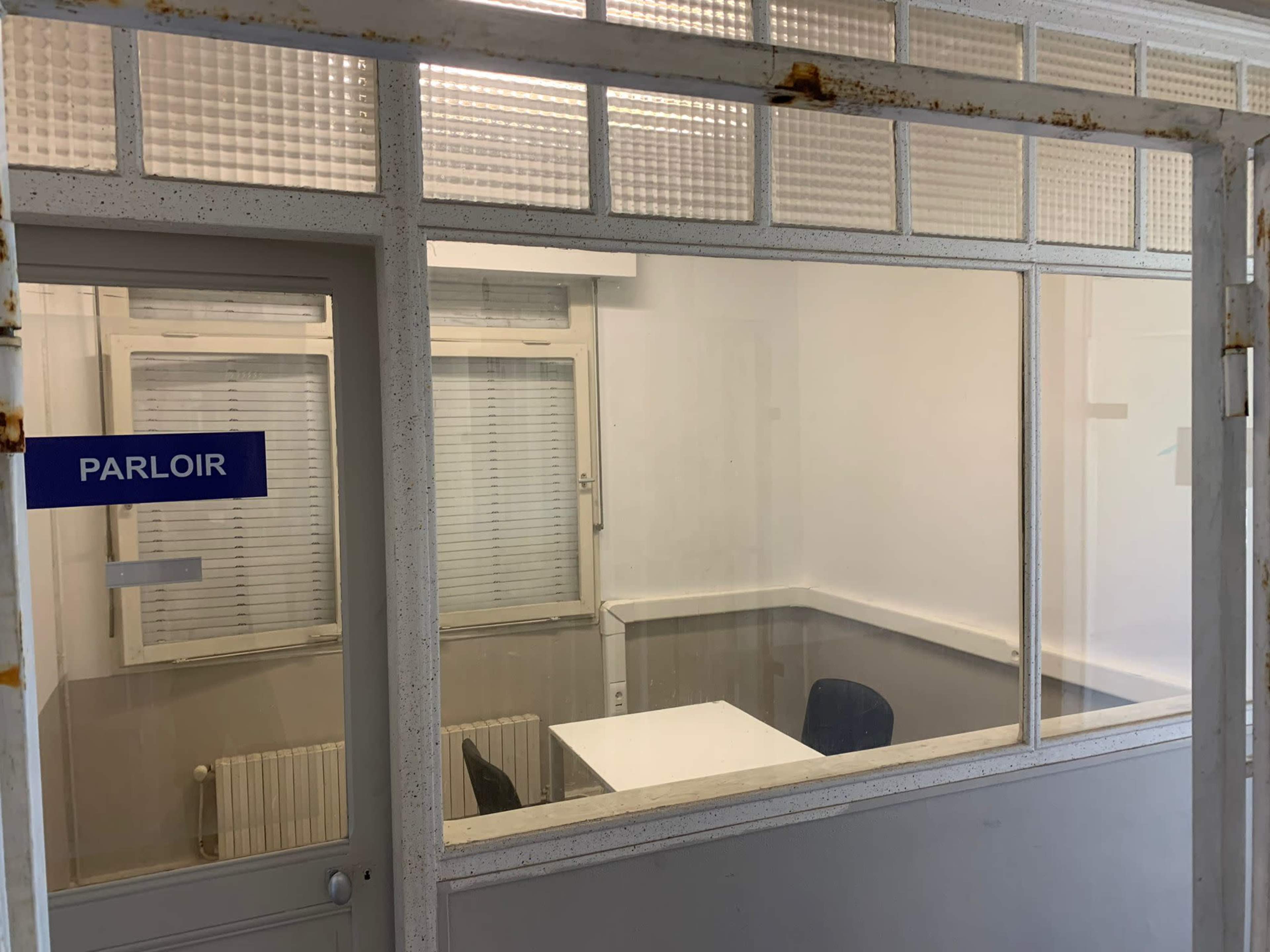 A small office with a white table and two chairs, visible through glass walls, labeled as "PARLOIR."