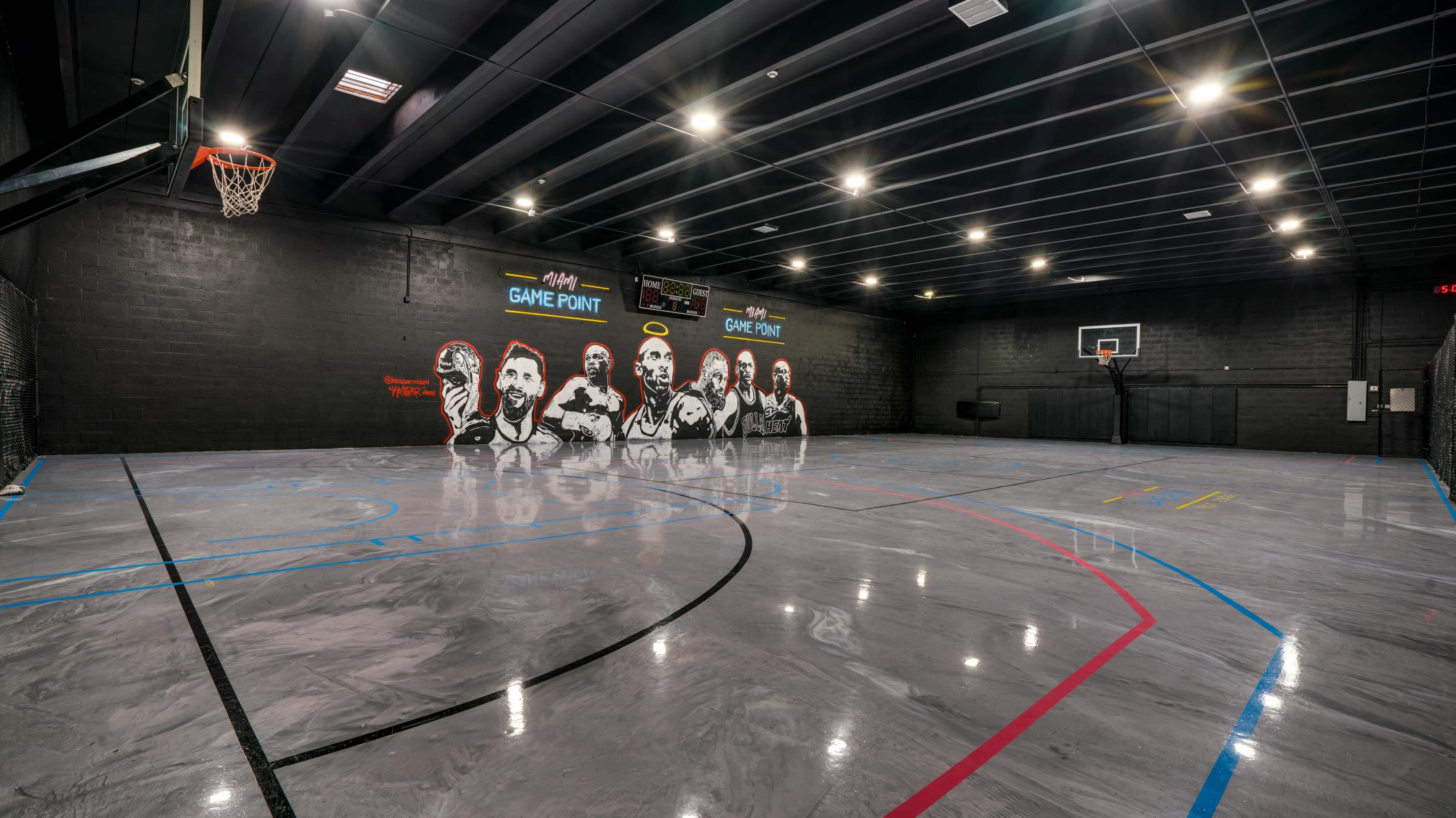 The image shows an indoor basketball court with a polished floor, black walls featuring mural art, and basketball hoops at each end.
