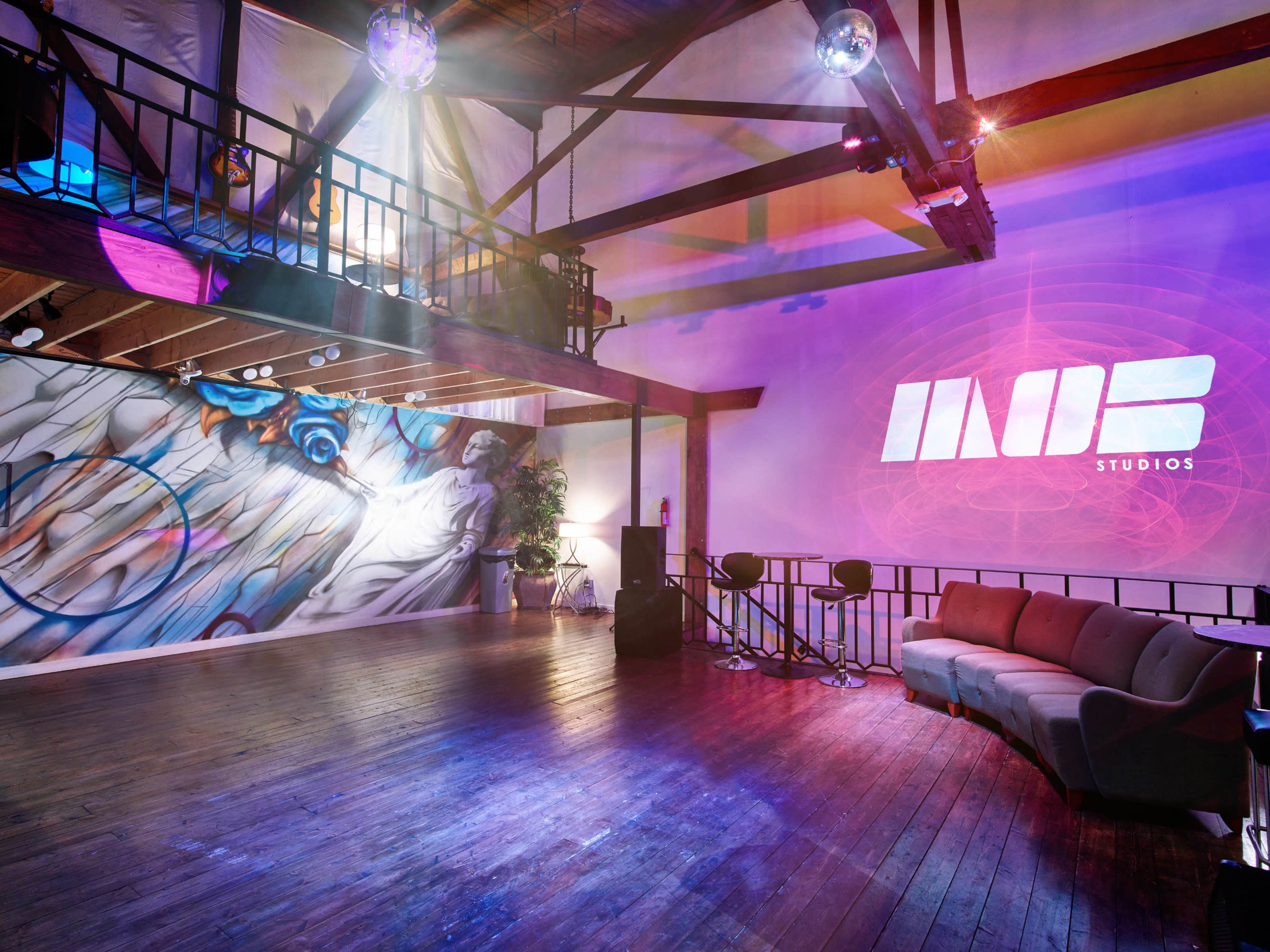 The interior of a spacious studio features a vibrant mural, modern seating, and a large projection displaying the logo "INOB STUDIOS."