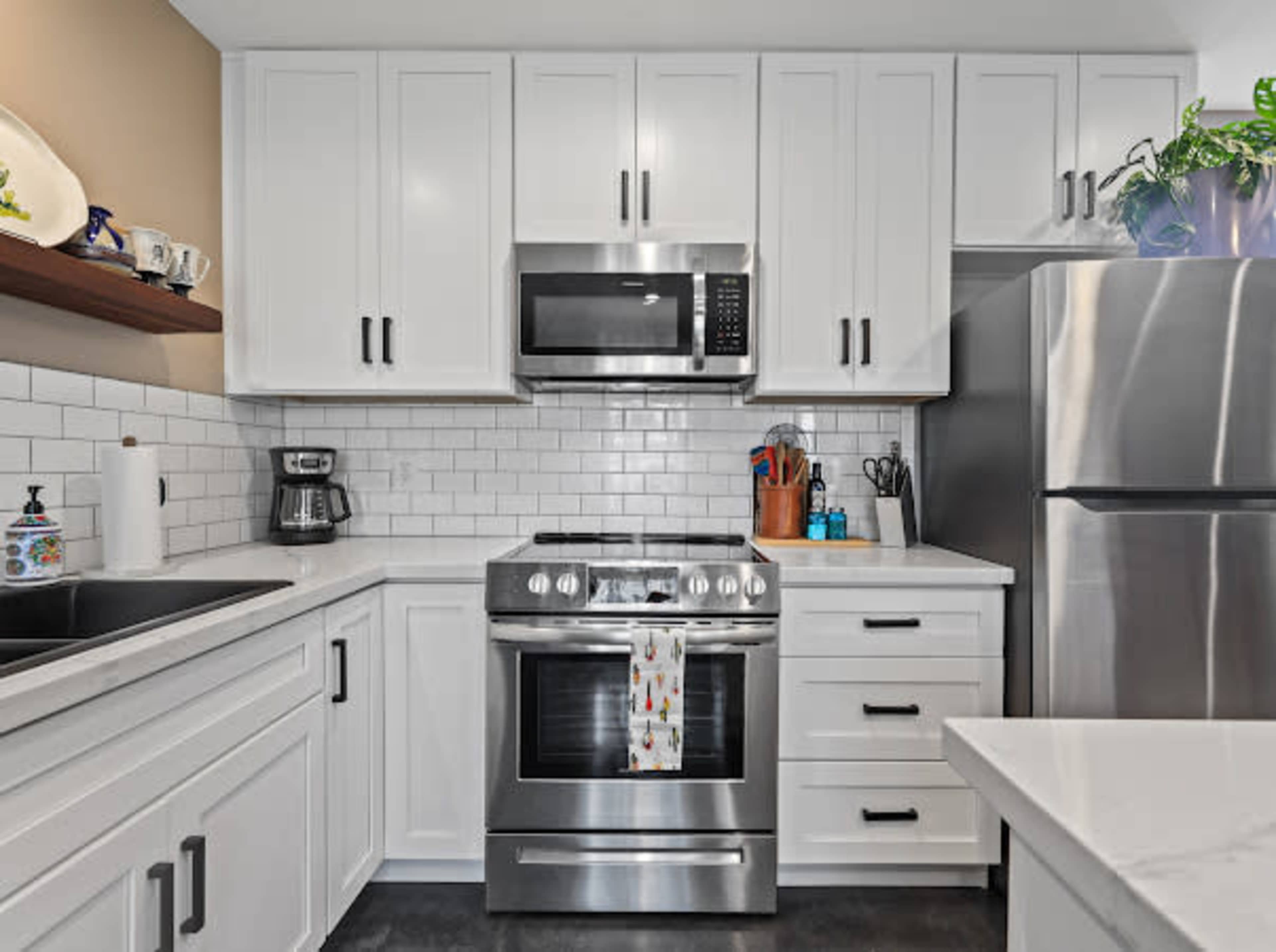 The image shows a modern kitchen with white cabinetry, a stainless steel oven and refrigerator, and a tiled backsplash.