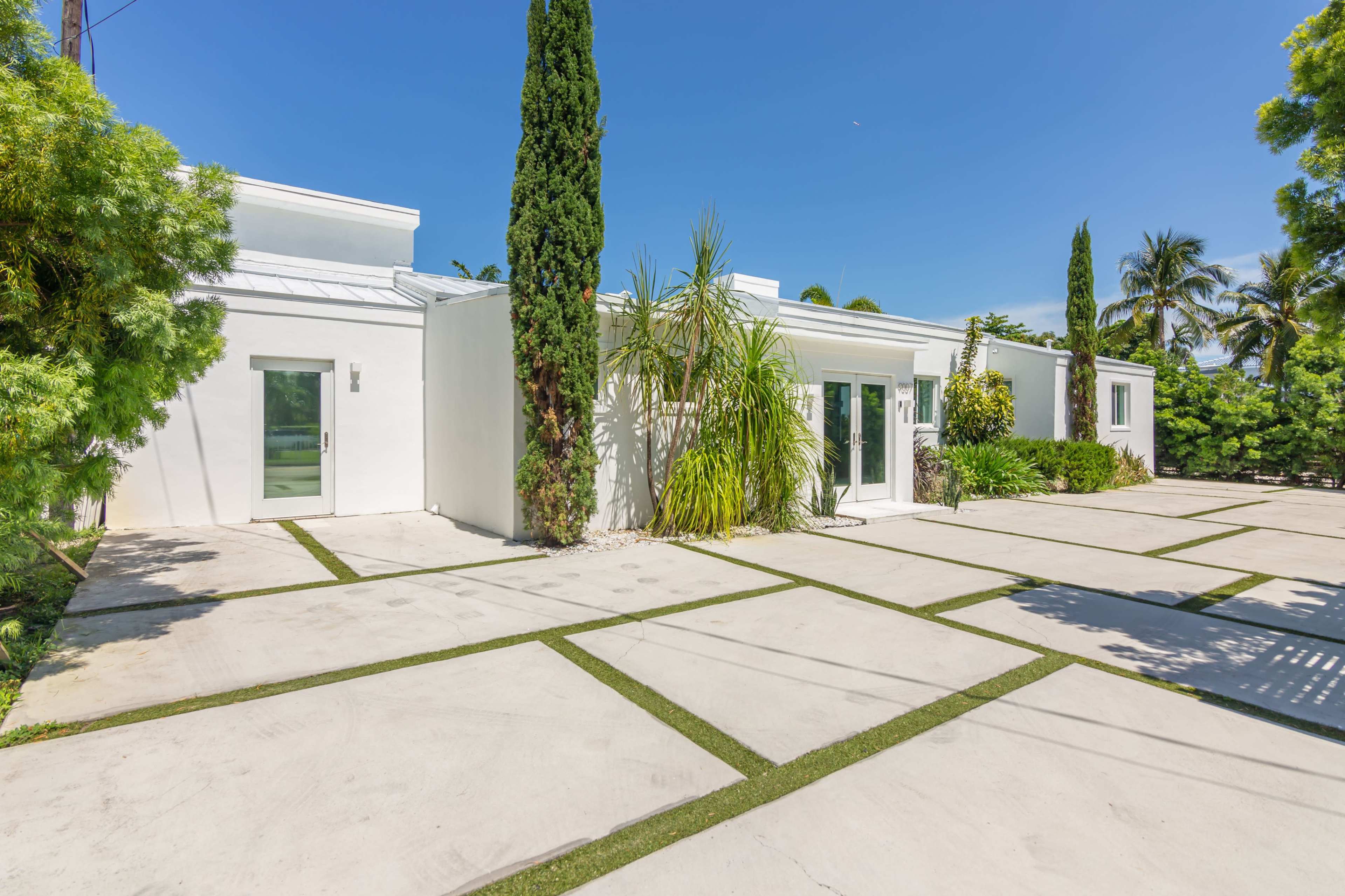 A modern white building surrounded by neatly arranged concrete slabs and greenery, under a clear blue sky.