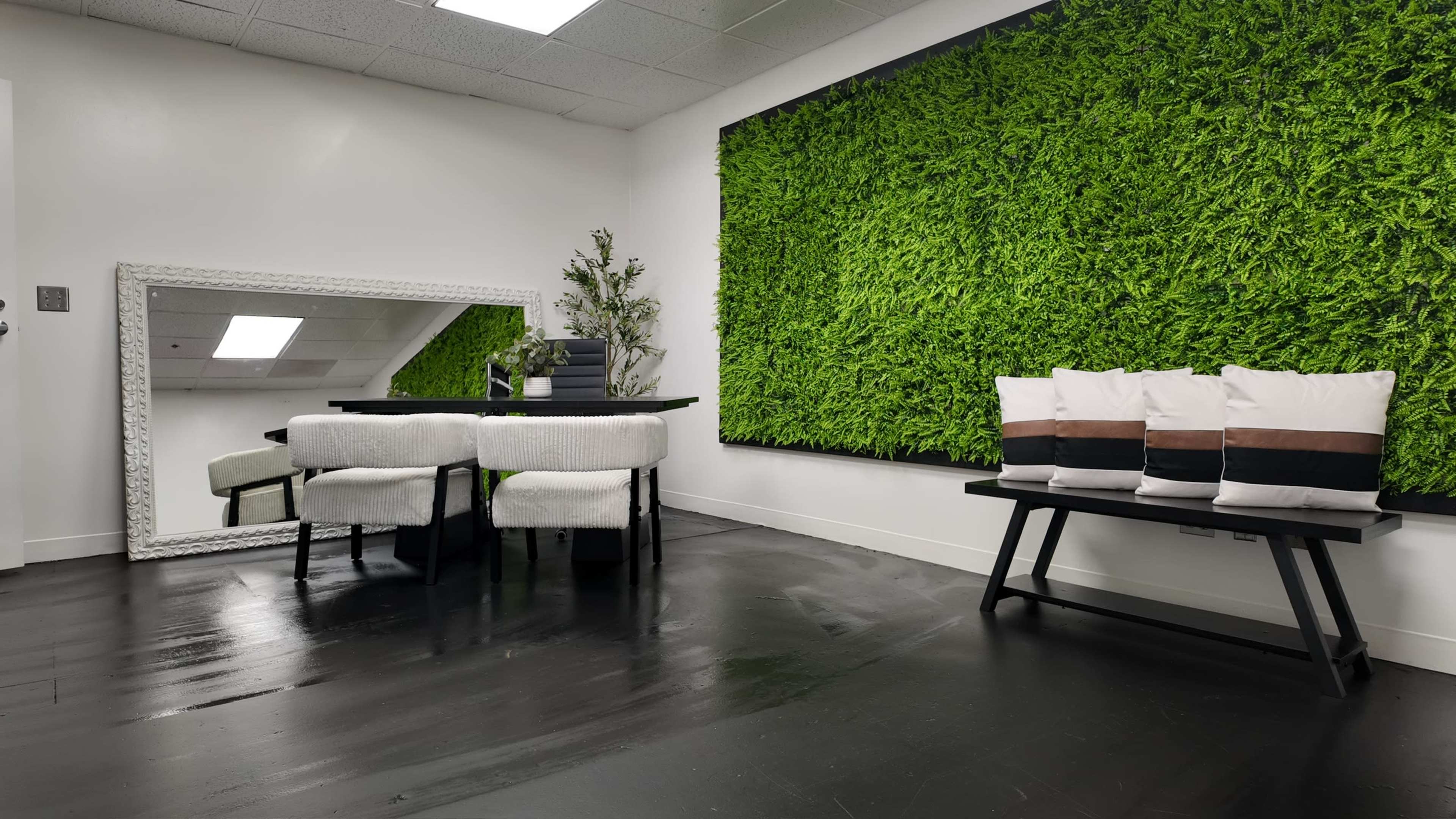 The image shows a modern interior space featuring a table with chairs, a large mirror, a decorative plant, and a green moss wall.