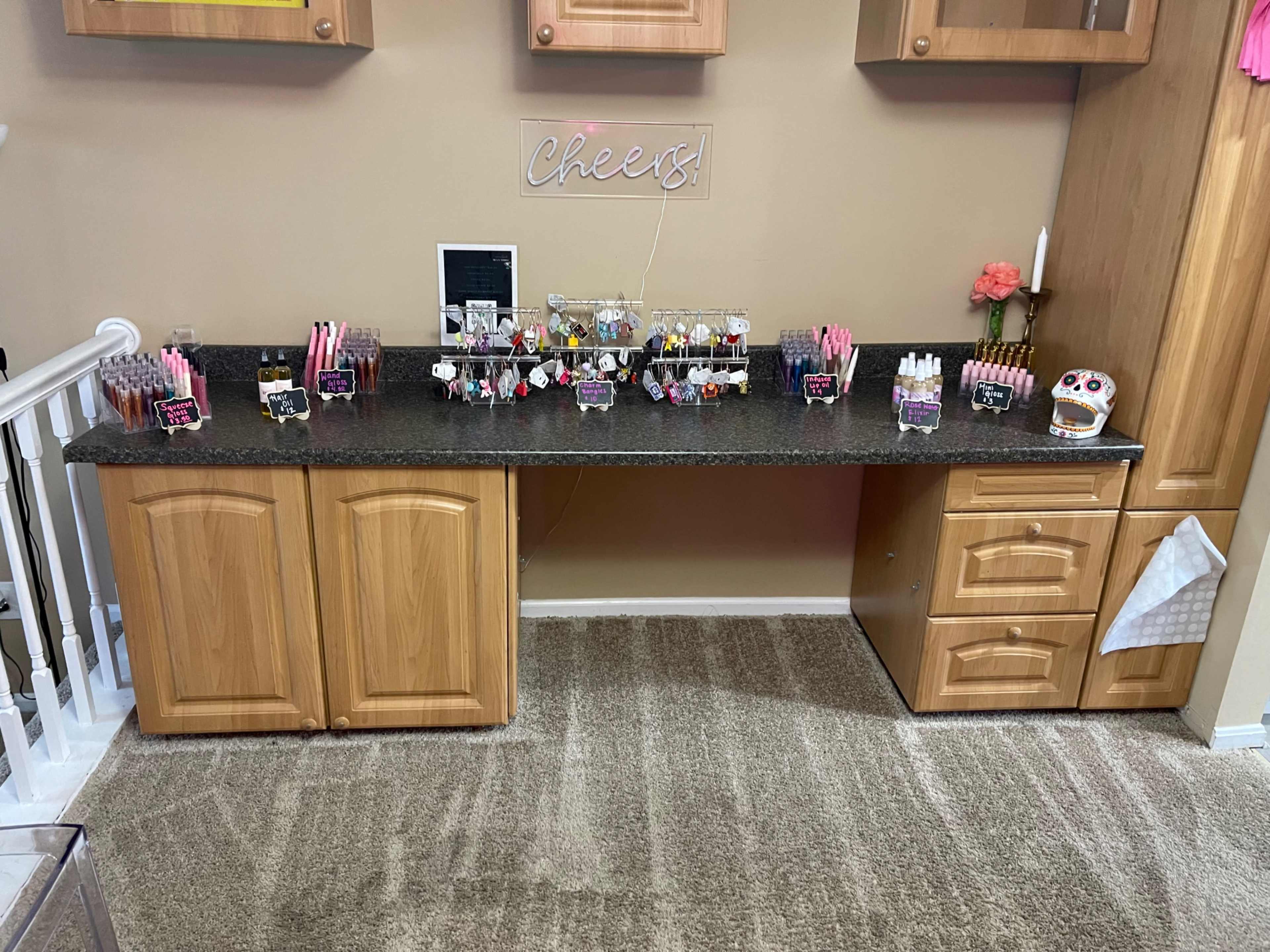 A countertop is lined with various beauty products organized in clear containers, situated beneath wooden cabinetry against a wall.
