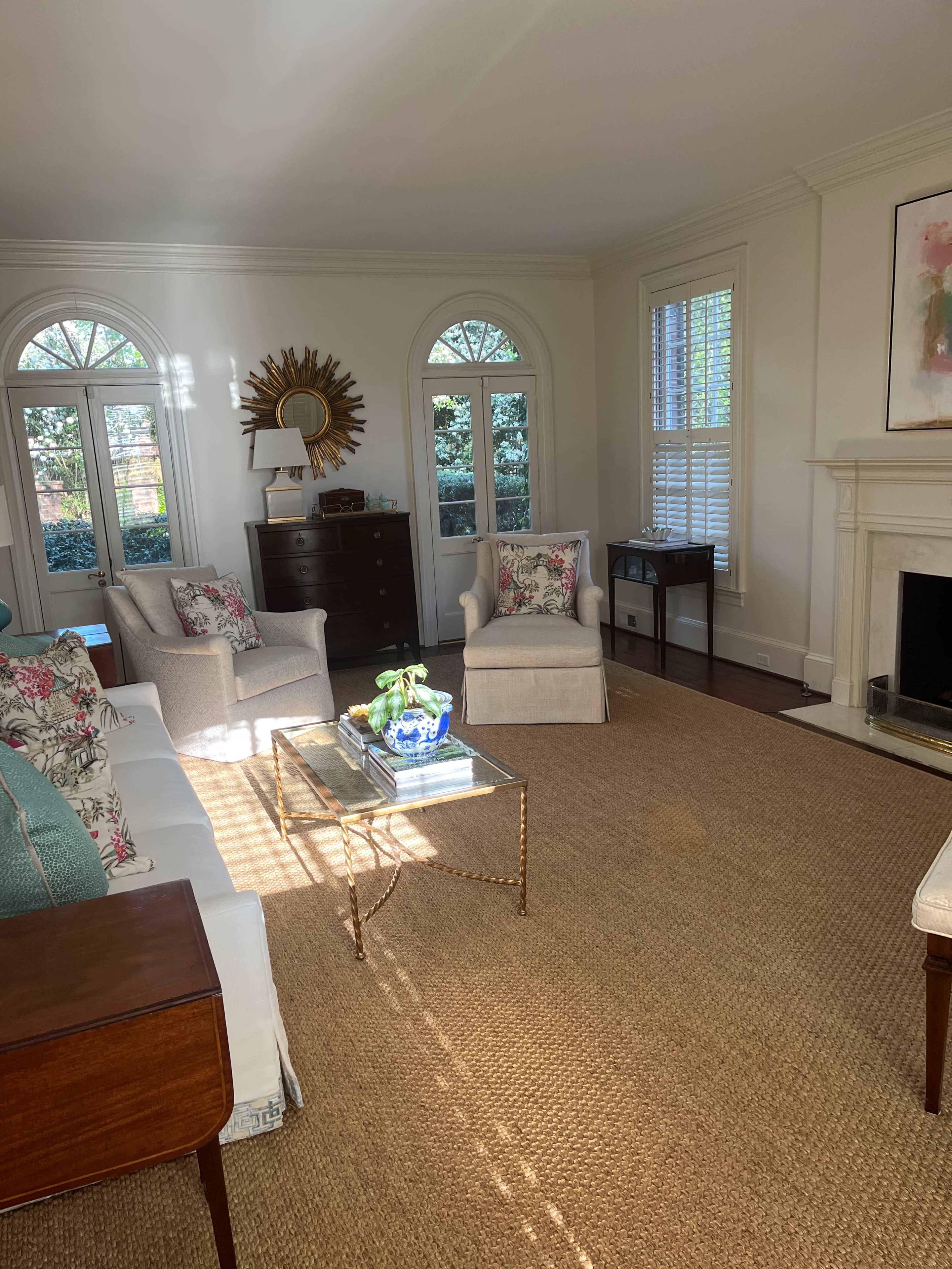 The living room features a light-colored sofa and armchairs around a coffee table, with large windows allowing natural light to illuminate the space.