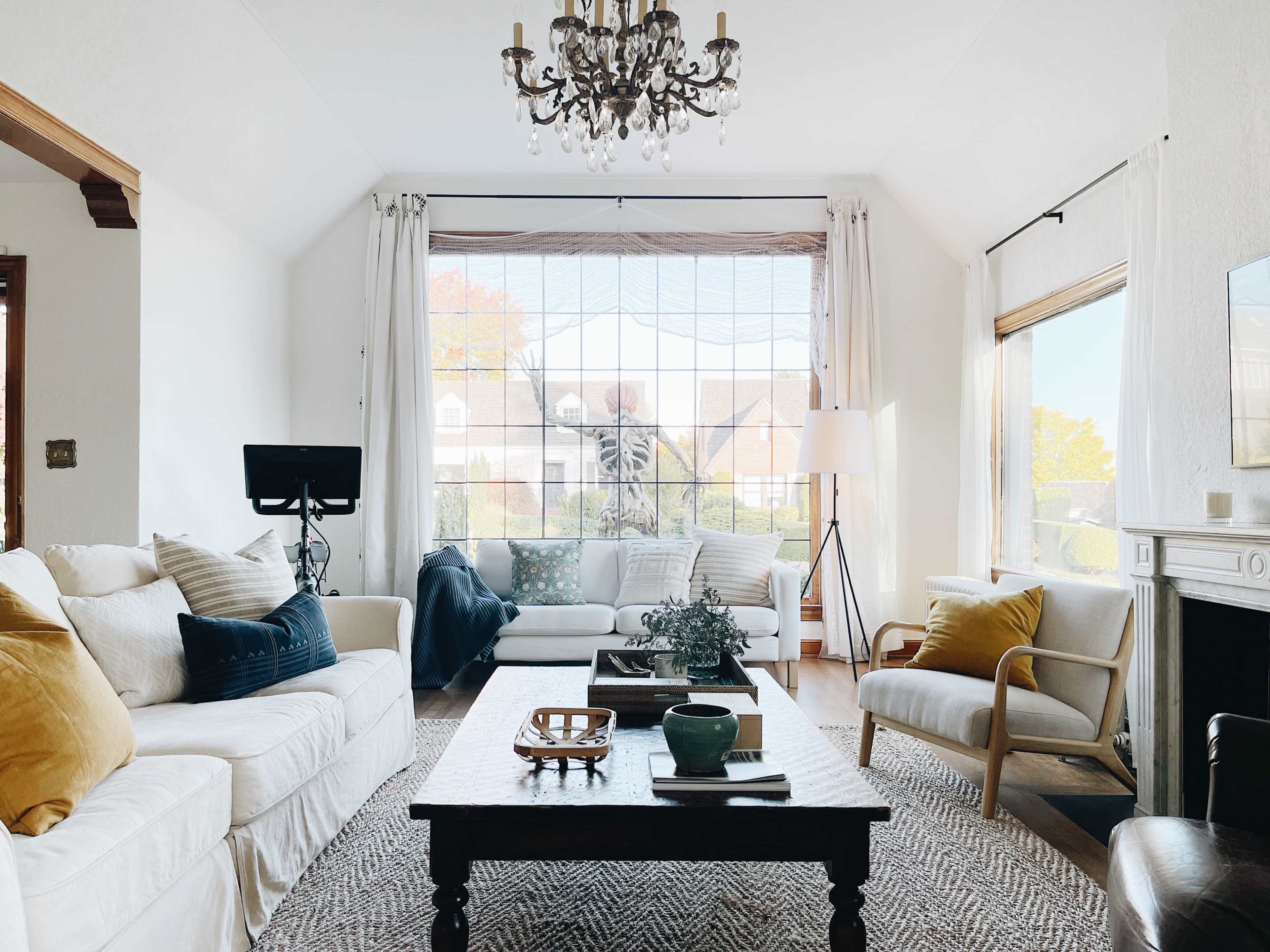 The living room features a white couch, a wooden coffee table, and large windows with light filtering through sheer curtains.