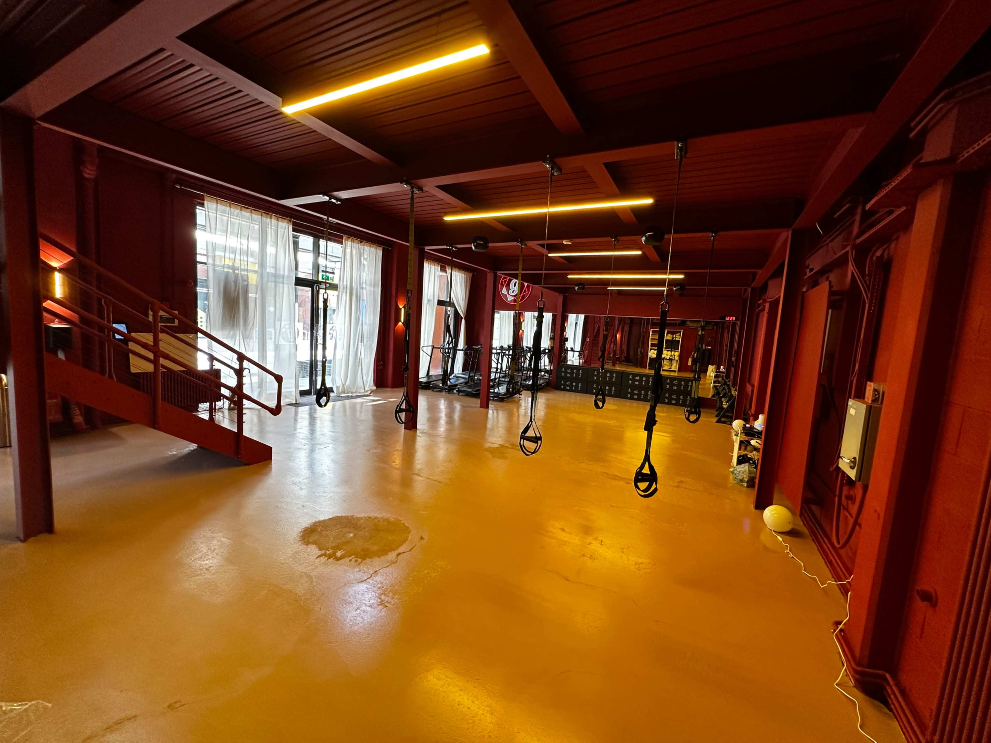 The image shows an empty gym interior with red walls, wooden ceiling beams, and suspension training straps hanging from the ceiling.