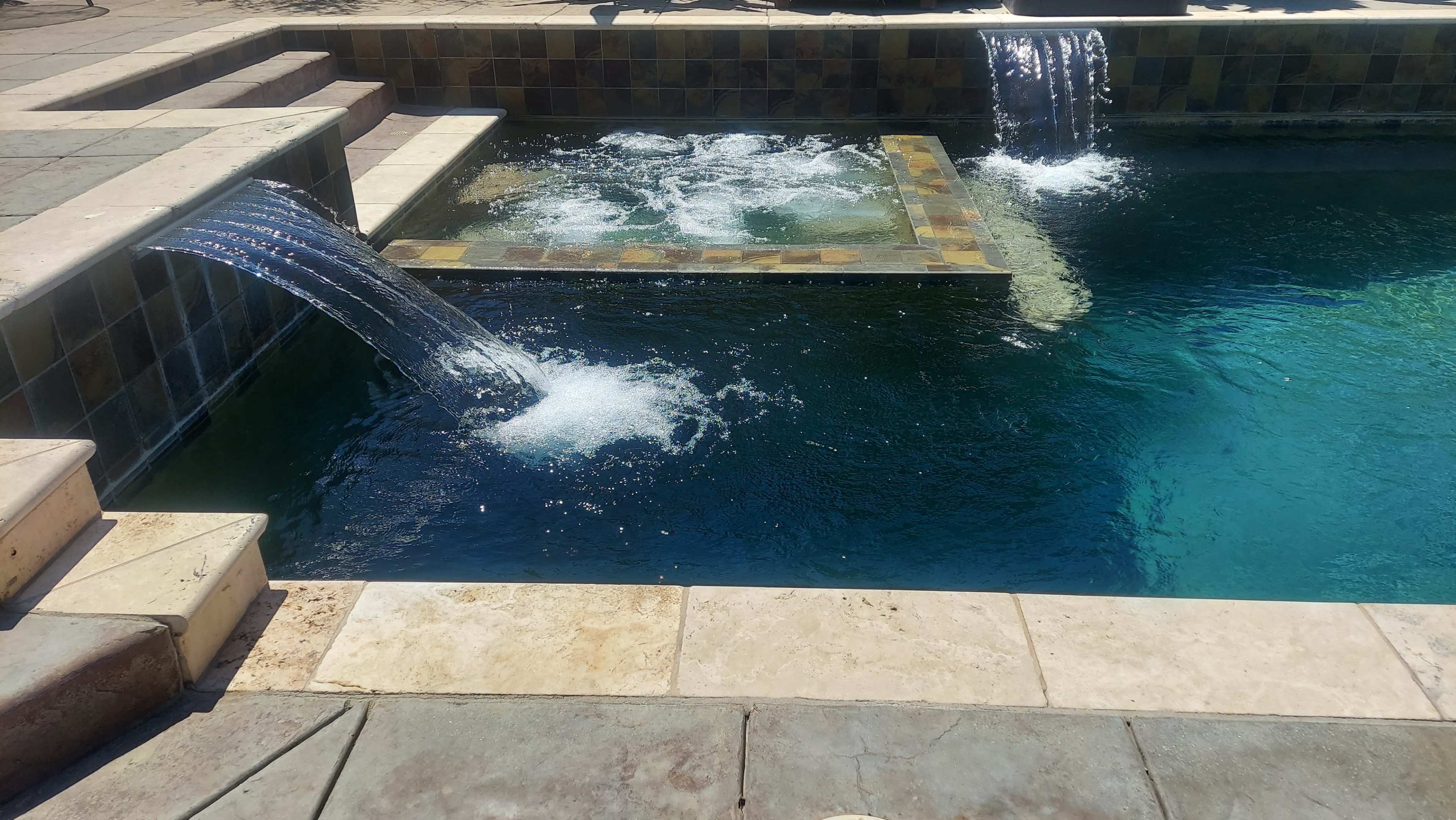 The image shows a swimming pool featuring two waterfall features cascading into the water.