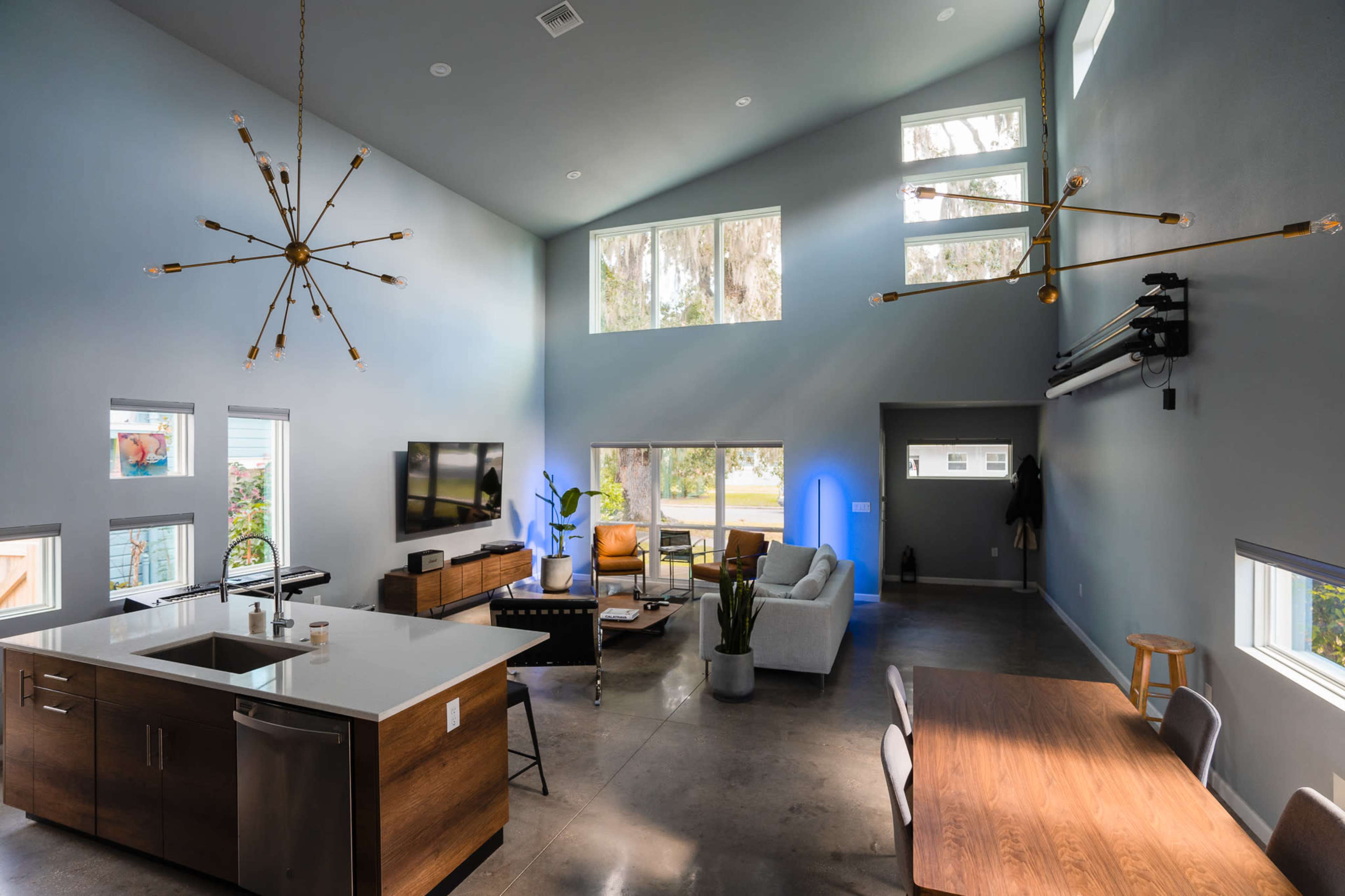 A modern living space with high ceilings, a kitchen island, a dining table, and large windows allowing for natural light.