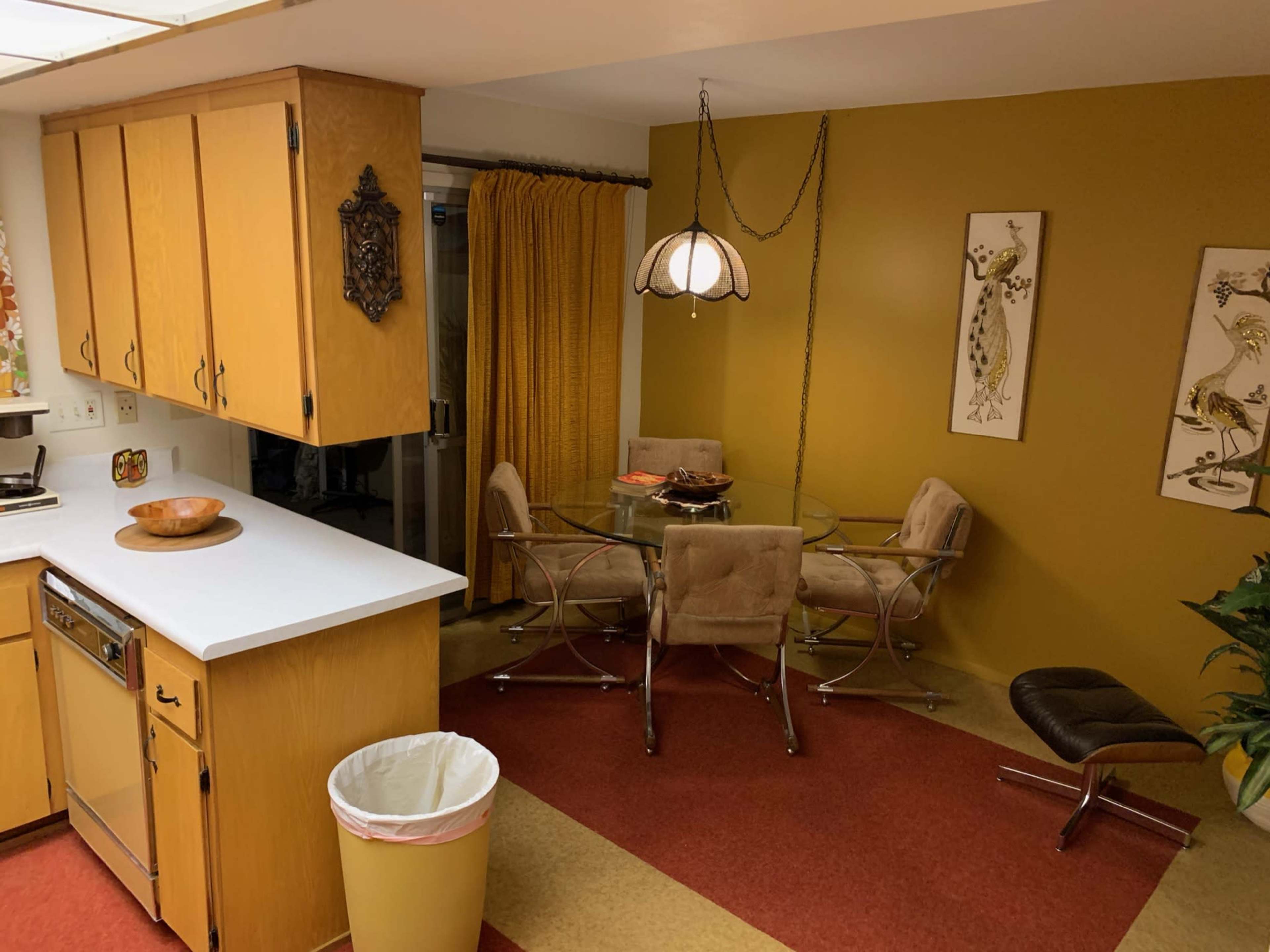 A kitchen area with yellow cabinets, a small round dining table surrounded by four chairs, and a large window with yellow curtains.