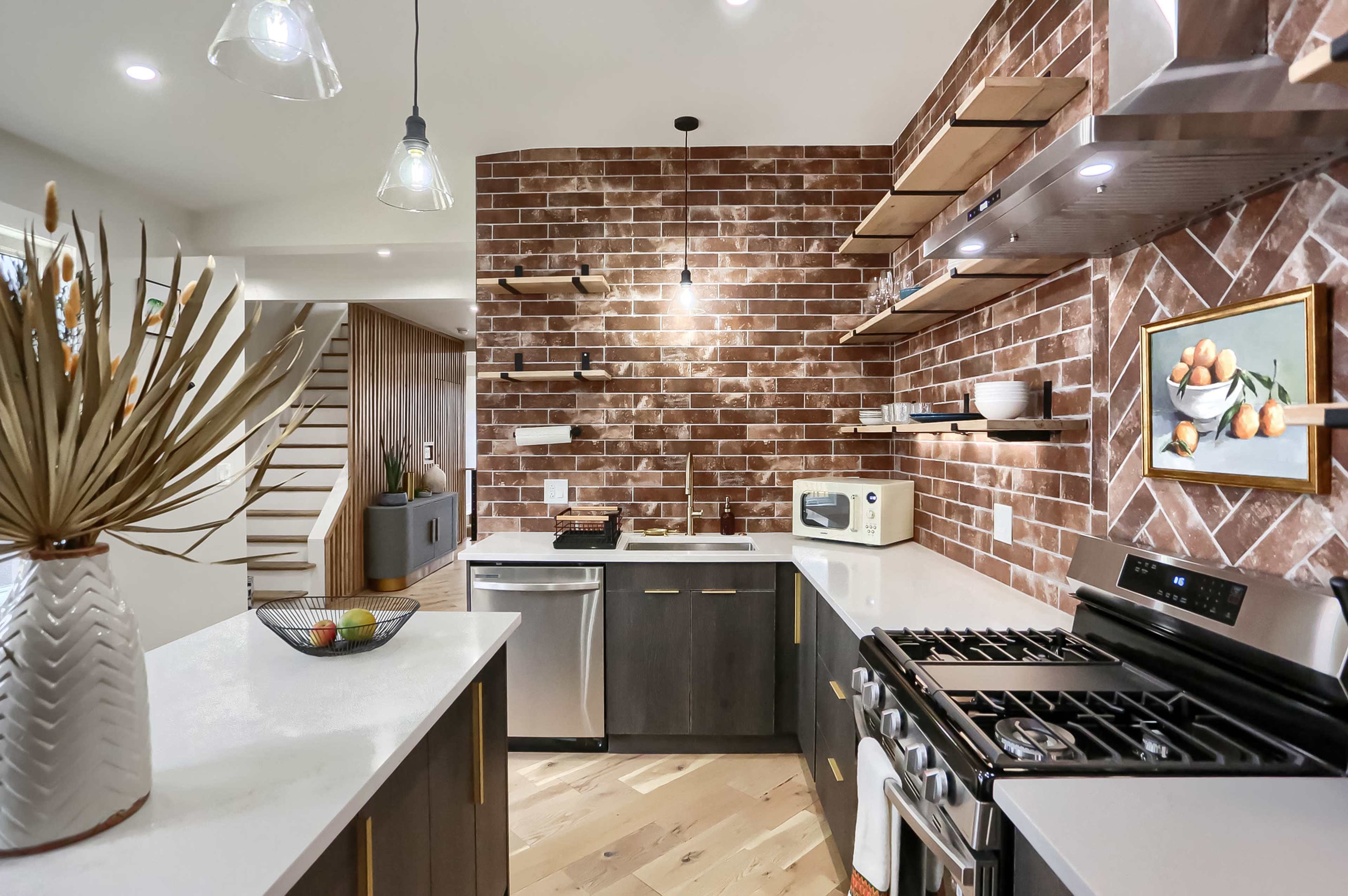 A modern kitchen features a brick accent wall, stainless steel appliances, and stylish open shelves displaying dishware.