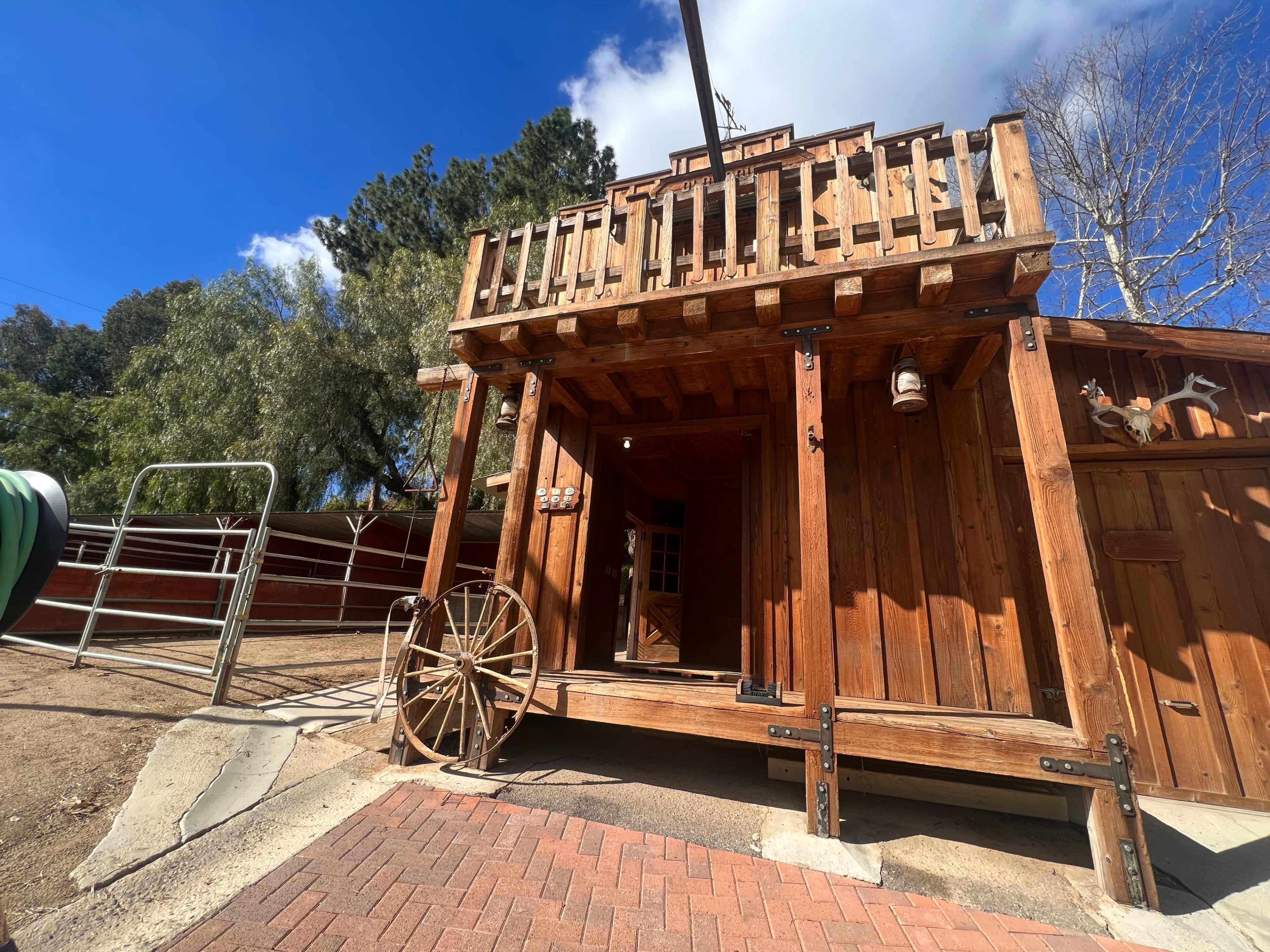 A wooden structure features a porch with railings and a wagon wheel beside the entrance.