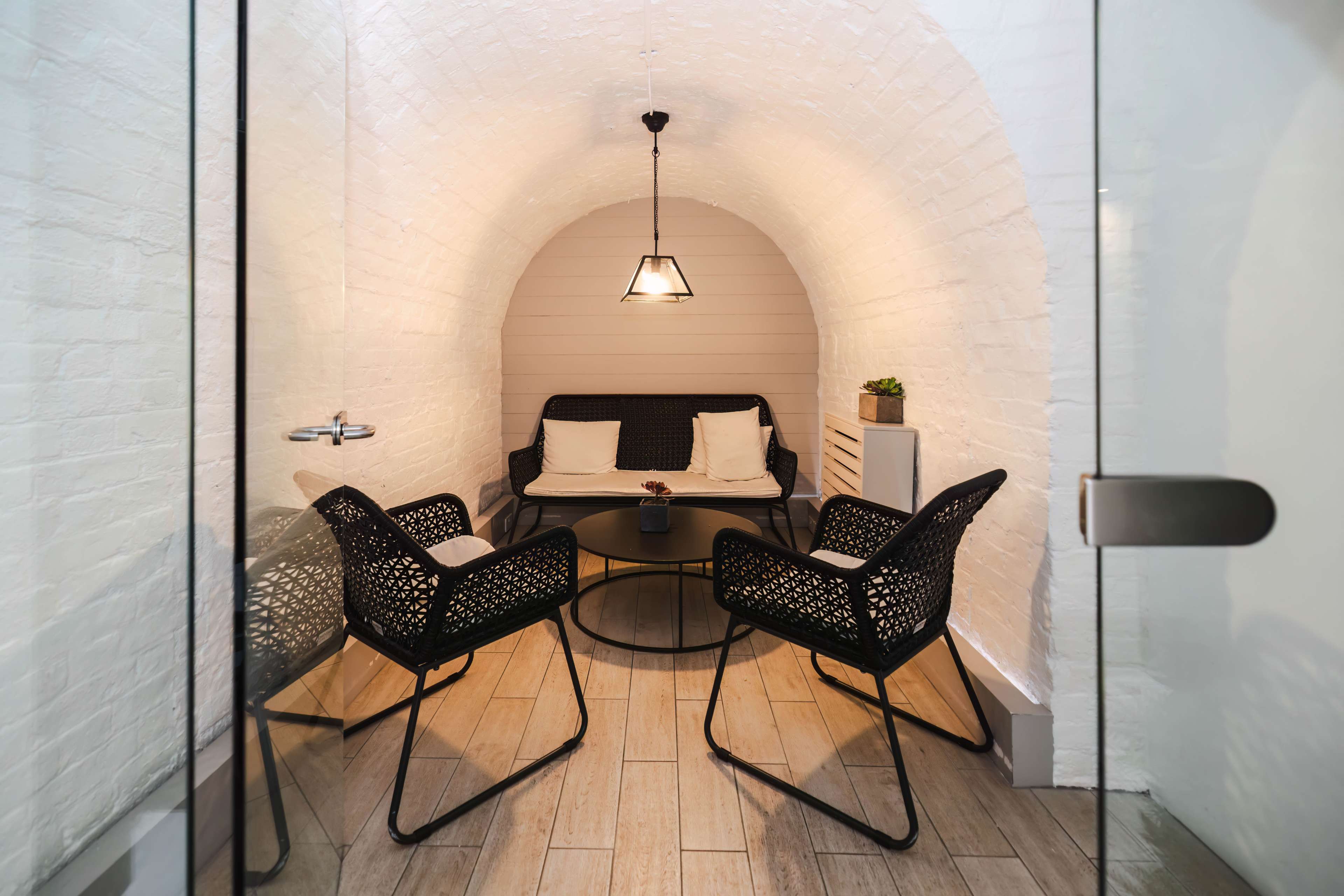 A small, semi-enclosed seating area with a table and four chairs, set within an arched white brick space.