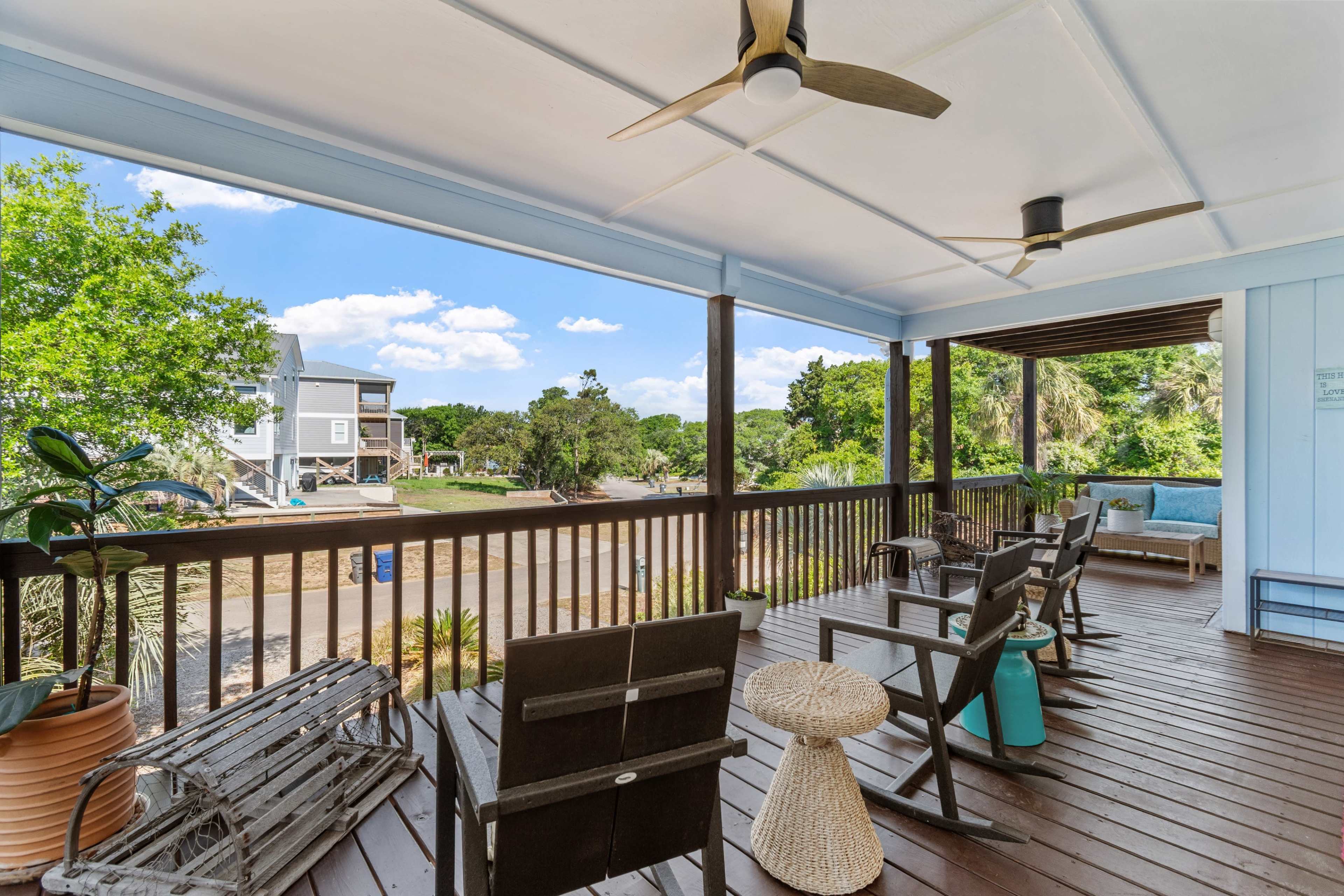 The image shows a spacious porch with wooden flooring, several seating options, and a view of the surrounding landscape and houses.