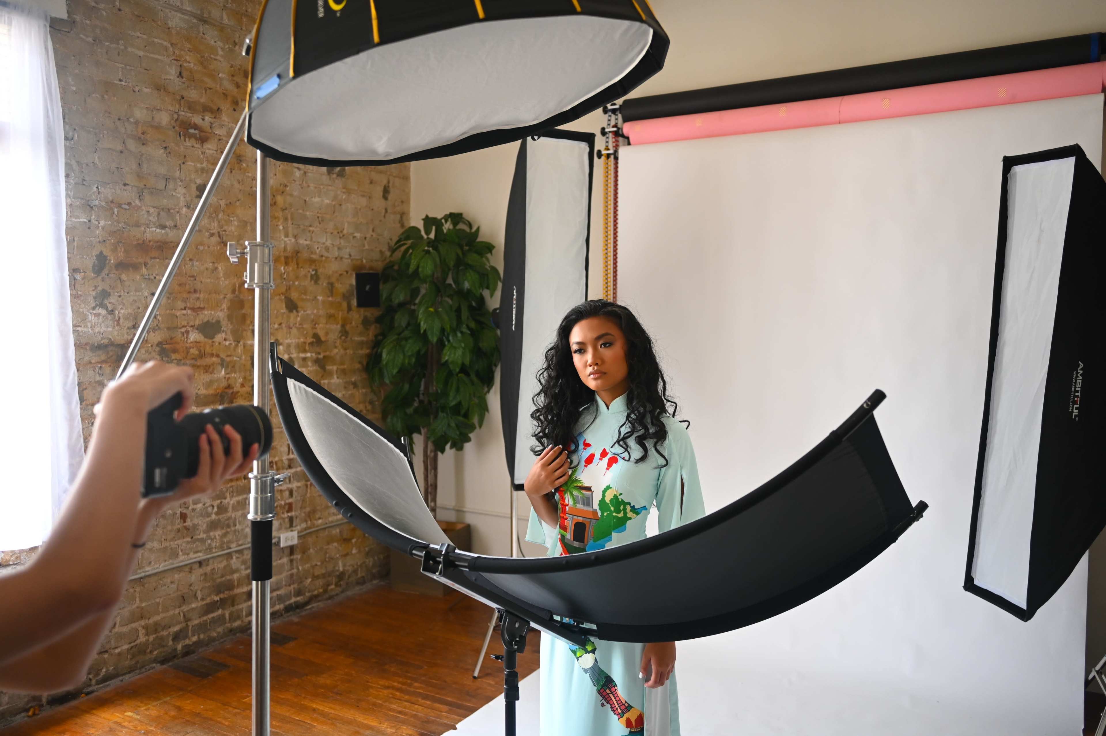 A model poses in front of a light setup on a photography studio backdrop.