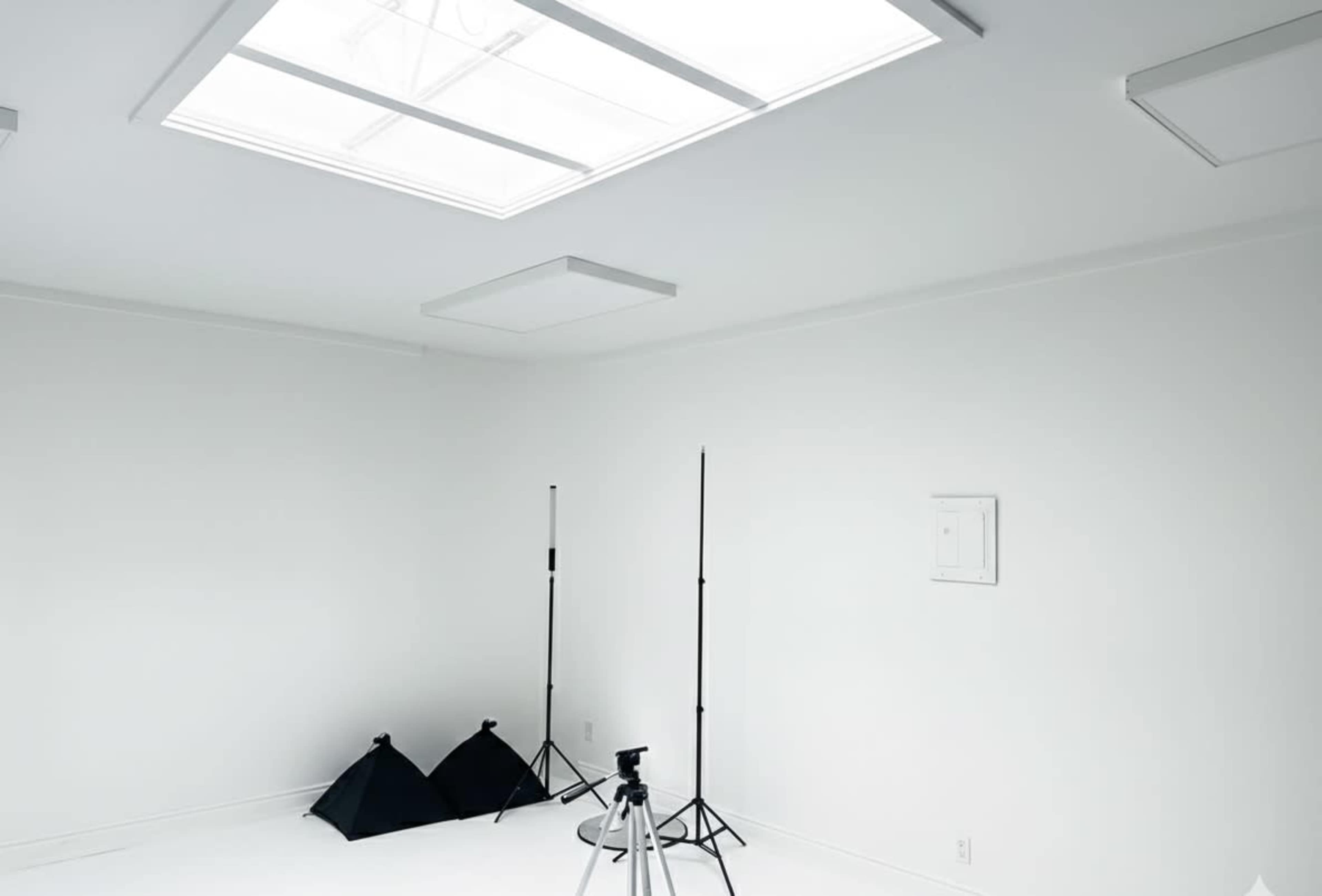 A white photography studio features two light stands, two softboxes, and a camera tripod in the corner.
