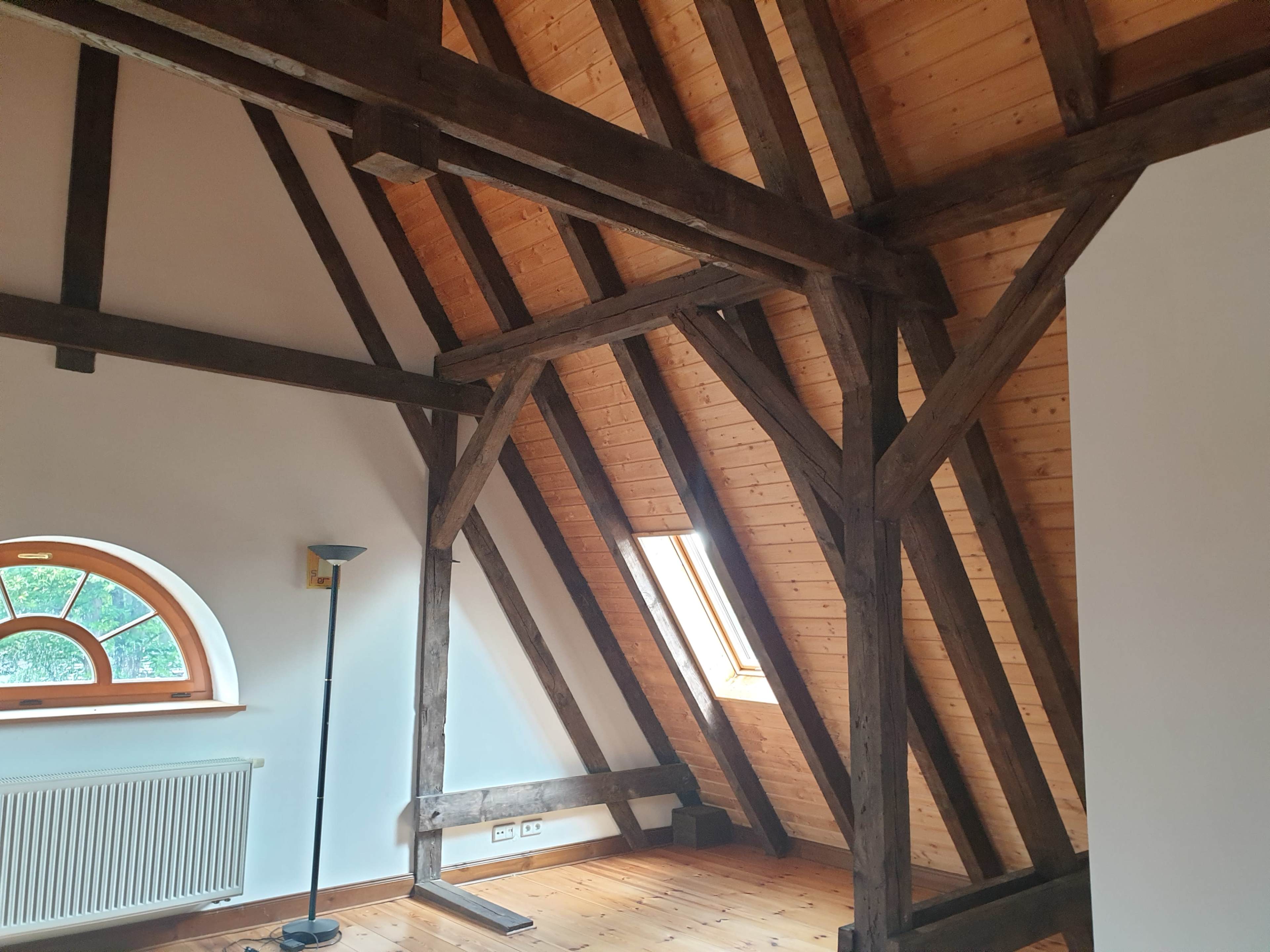 An attic room with exposed wooden beams, a sloped ceiling, a small window, and a floor lamp.