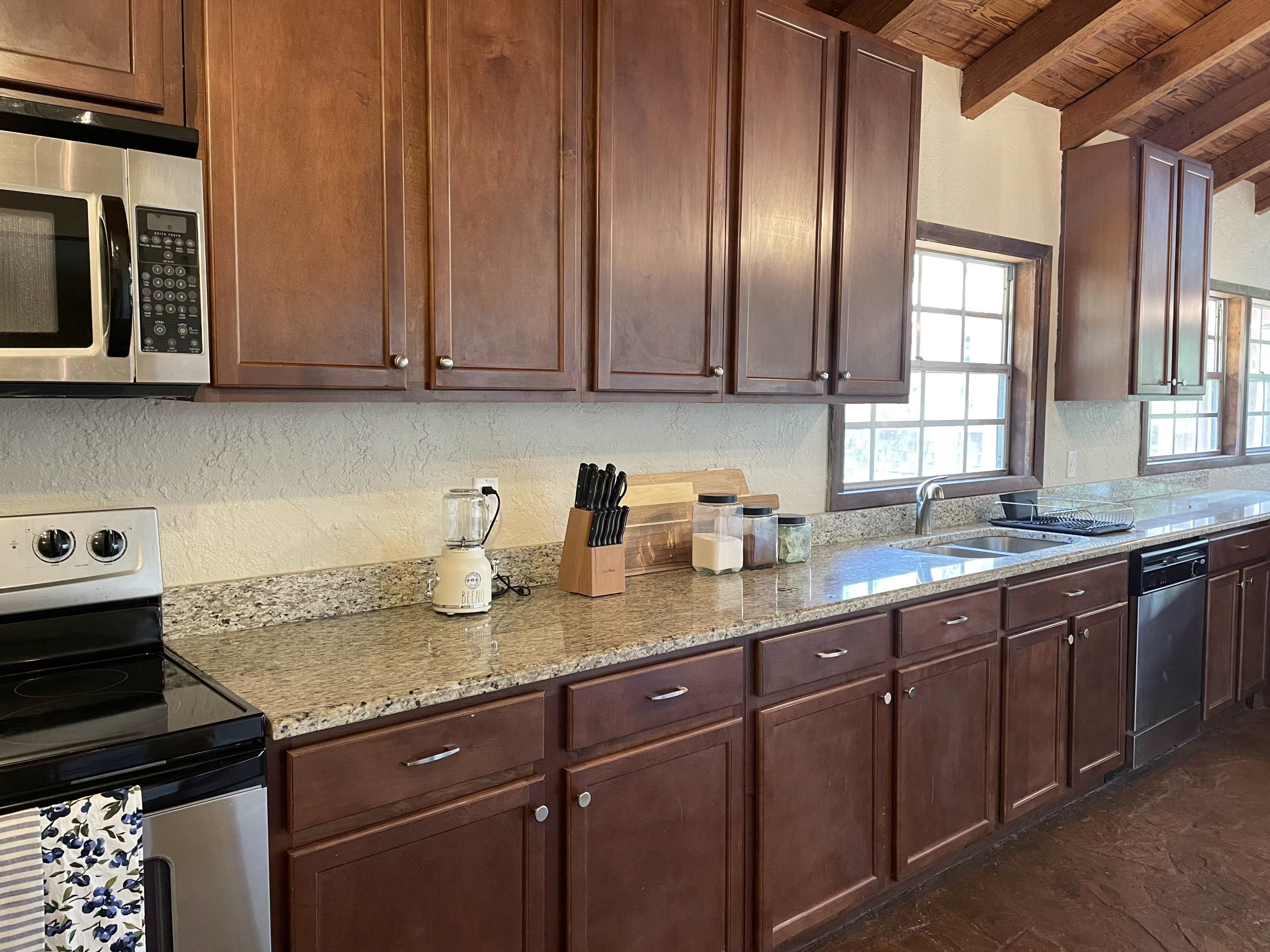 A modern kitchen features wooden cabinetry, granite countertops, and stainless steel appliances arranged along one side.