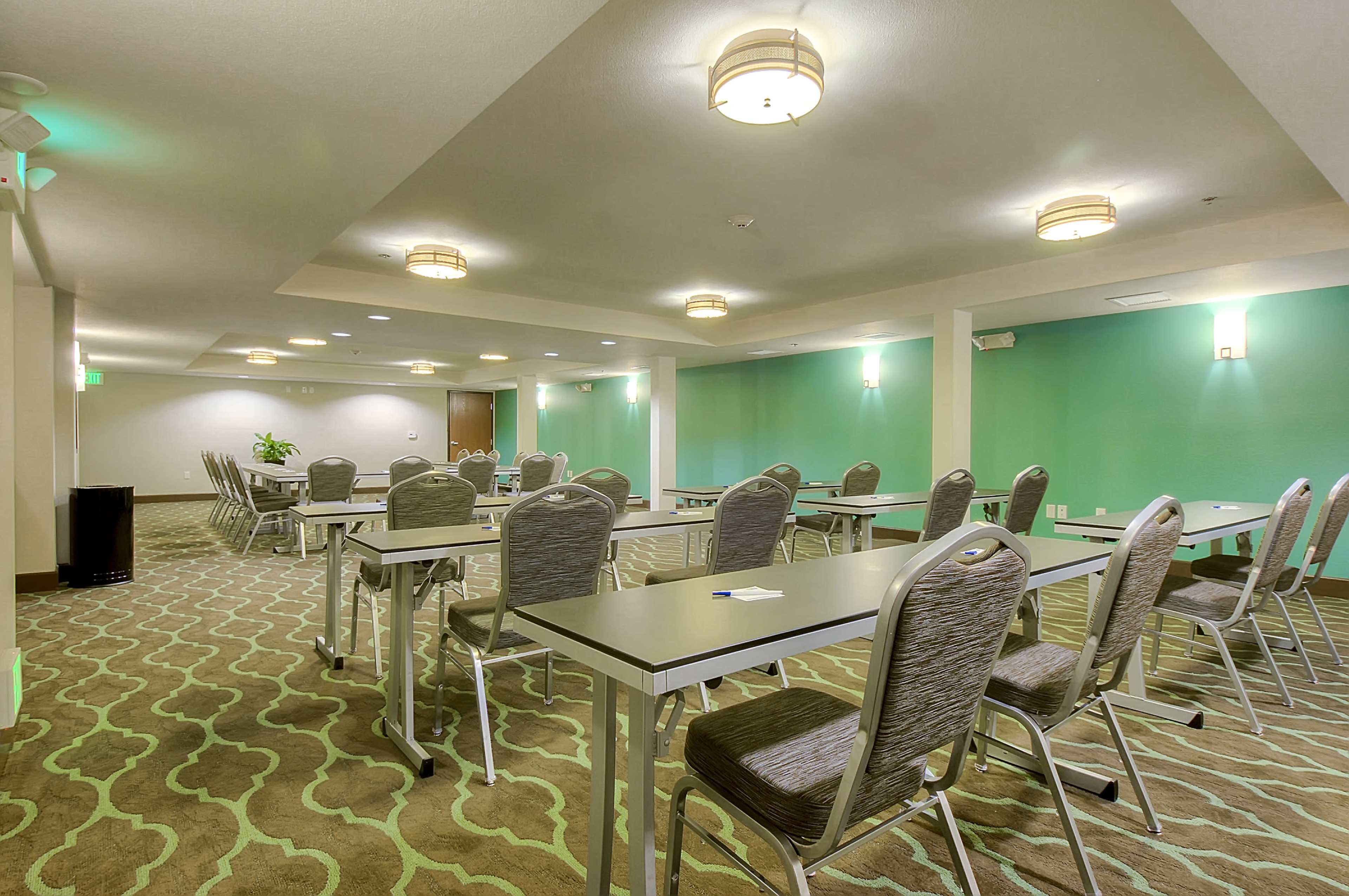 The image shows a conference room equipped with several rows of tables and chairs under recessed lighting and green walls.