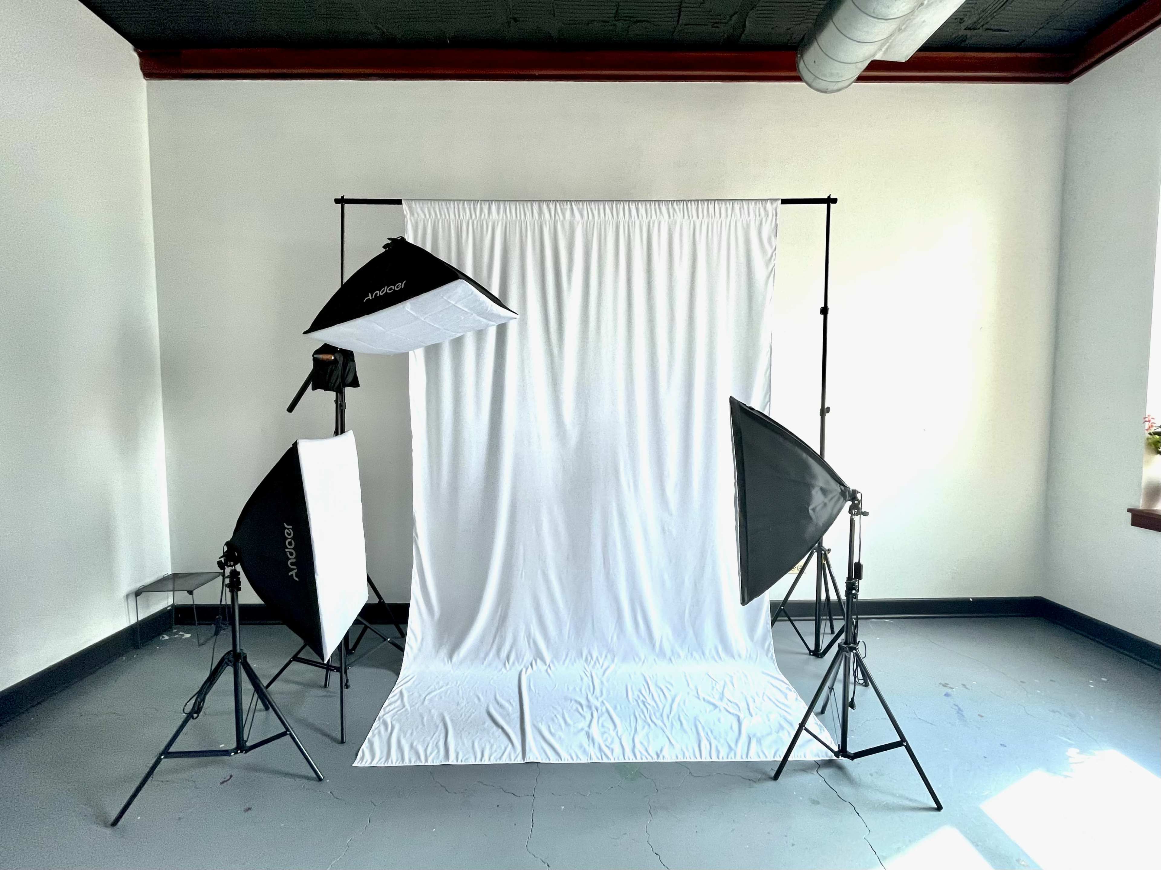 A photography studio setup with two softbox lights and a backdrop stand holding a white fabric.