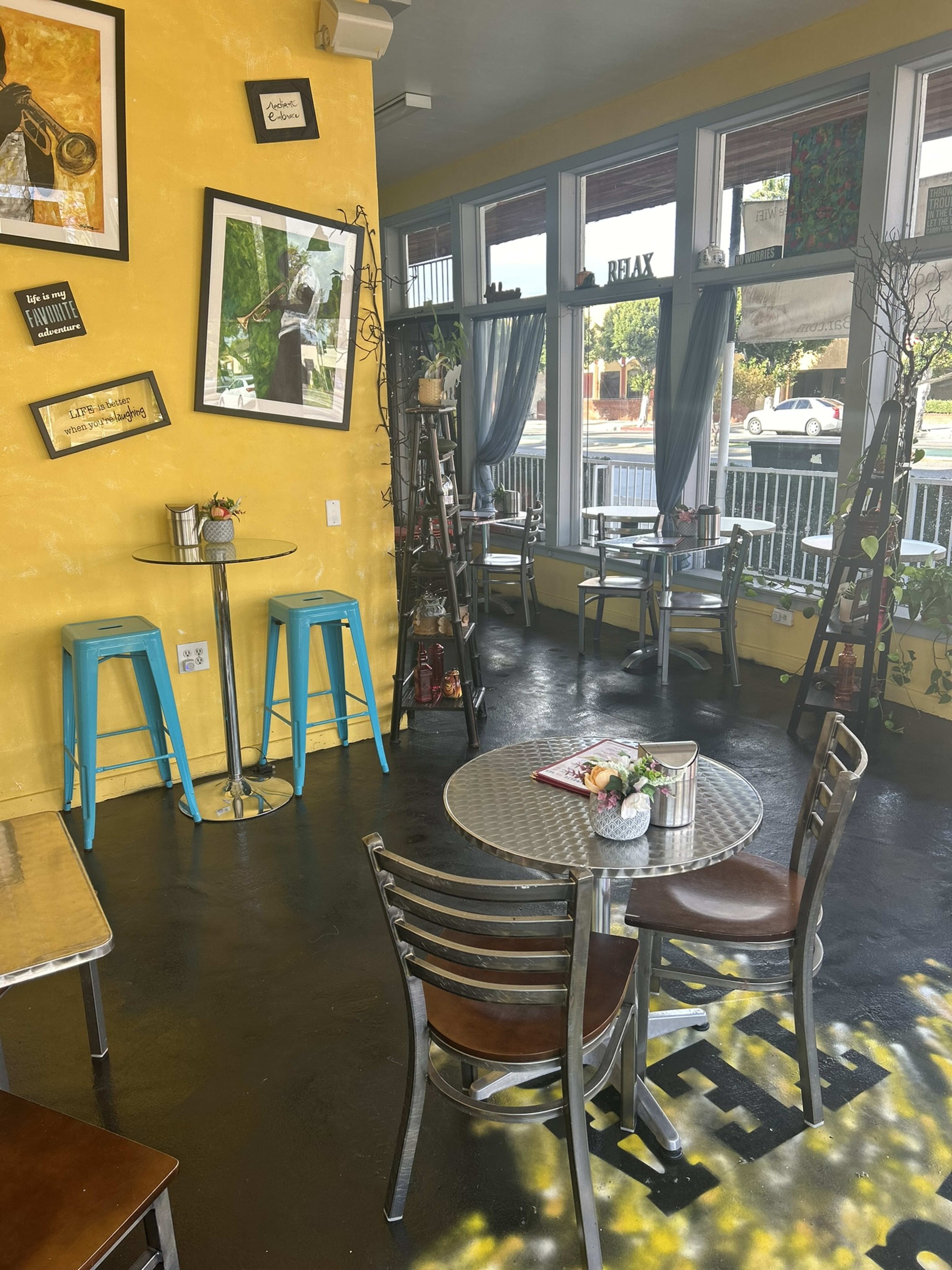 A café interior featuring yellow walls, metal tables with chairs, and shelves displaying decorative items.