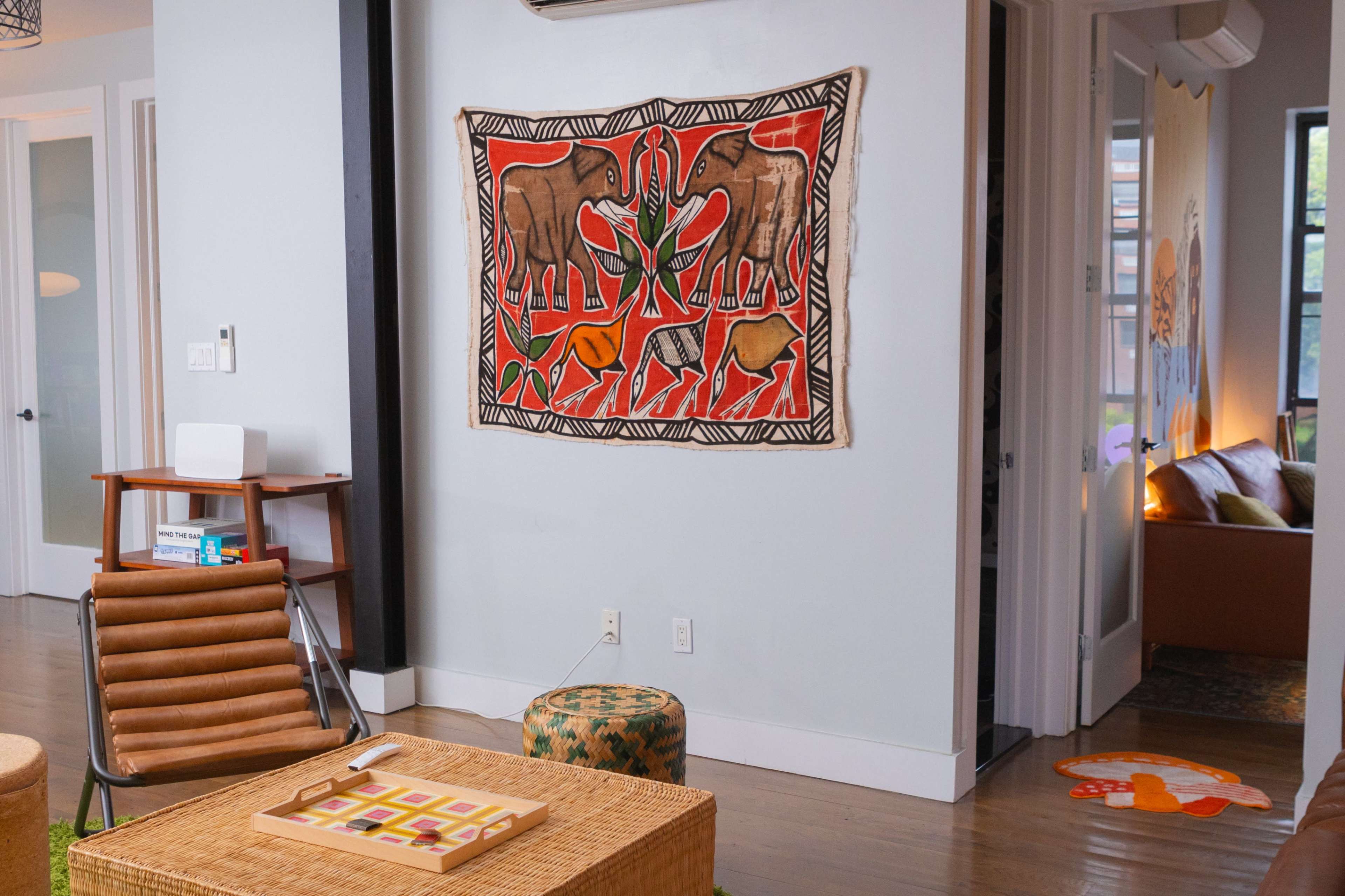 A cozy living space featuring a large elephant tapestry on the wall, a wicker coffee table, and a wooden chair.