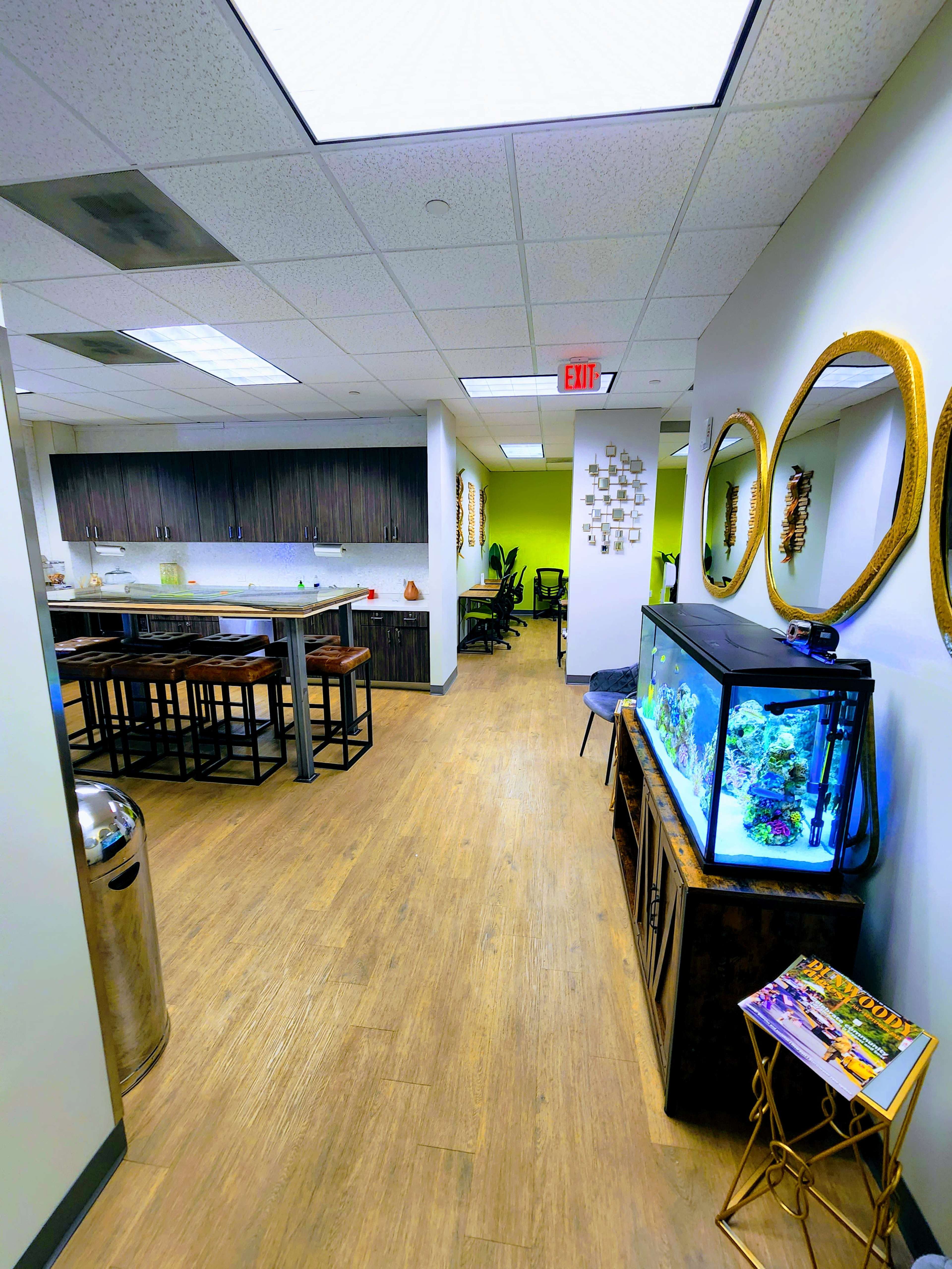 A modern office space features a kitchen area with bar seating, an aquarium, and decorative mirrors along the walls.