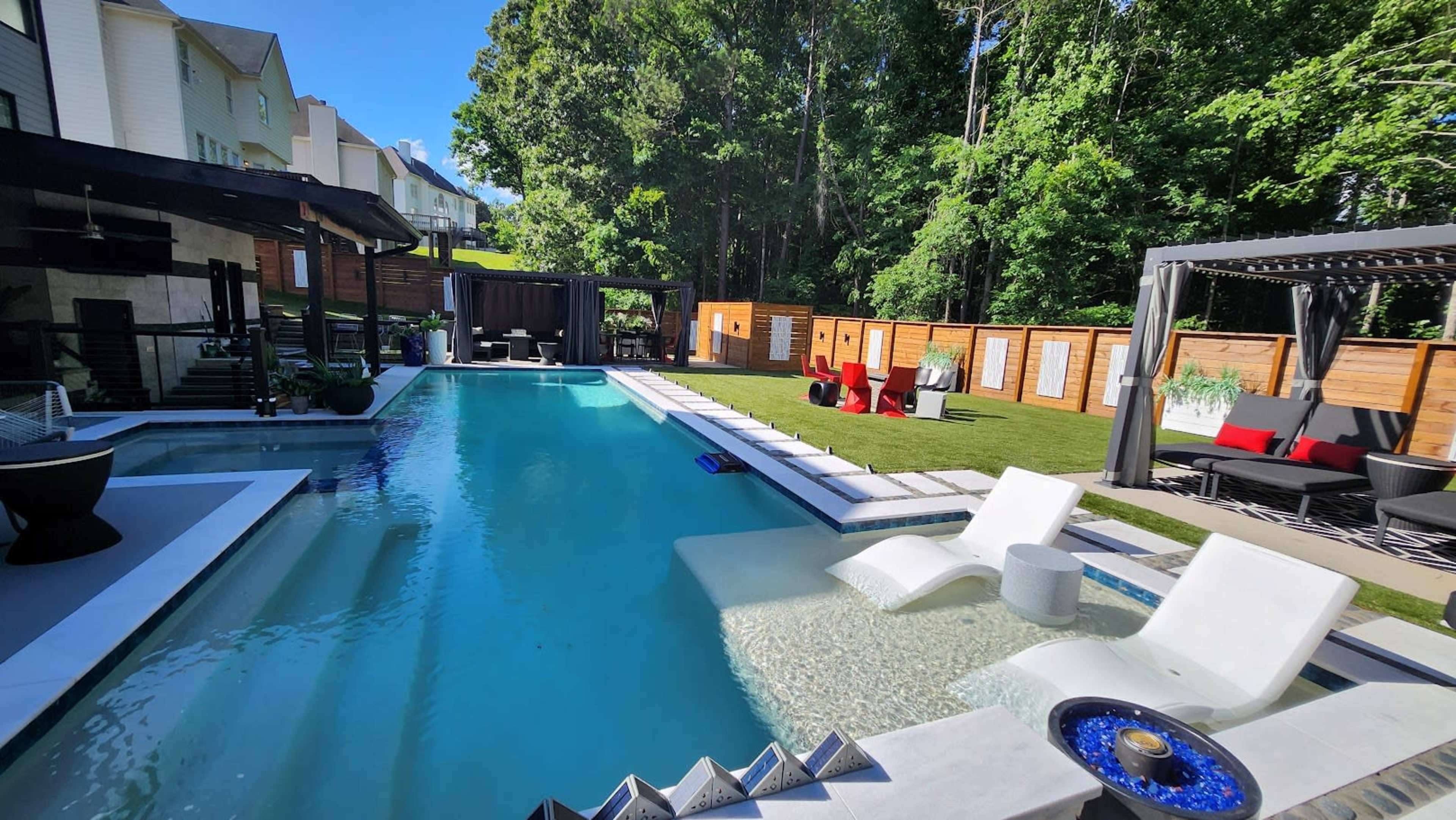 The image shows a backyard with a swimming pool, lounge chairs, and green landscaping, surrounded by wooden fencing and seating areas.