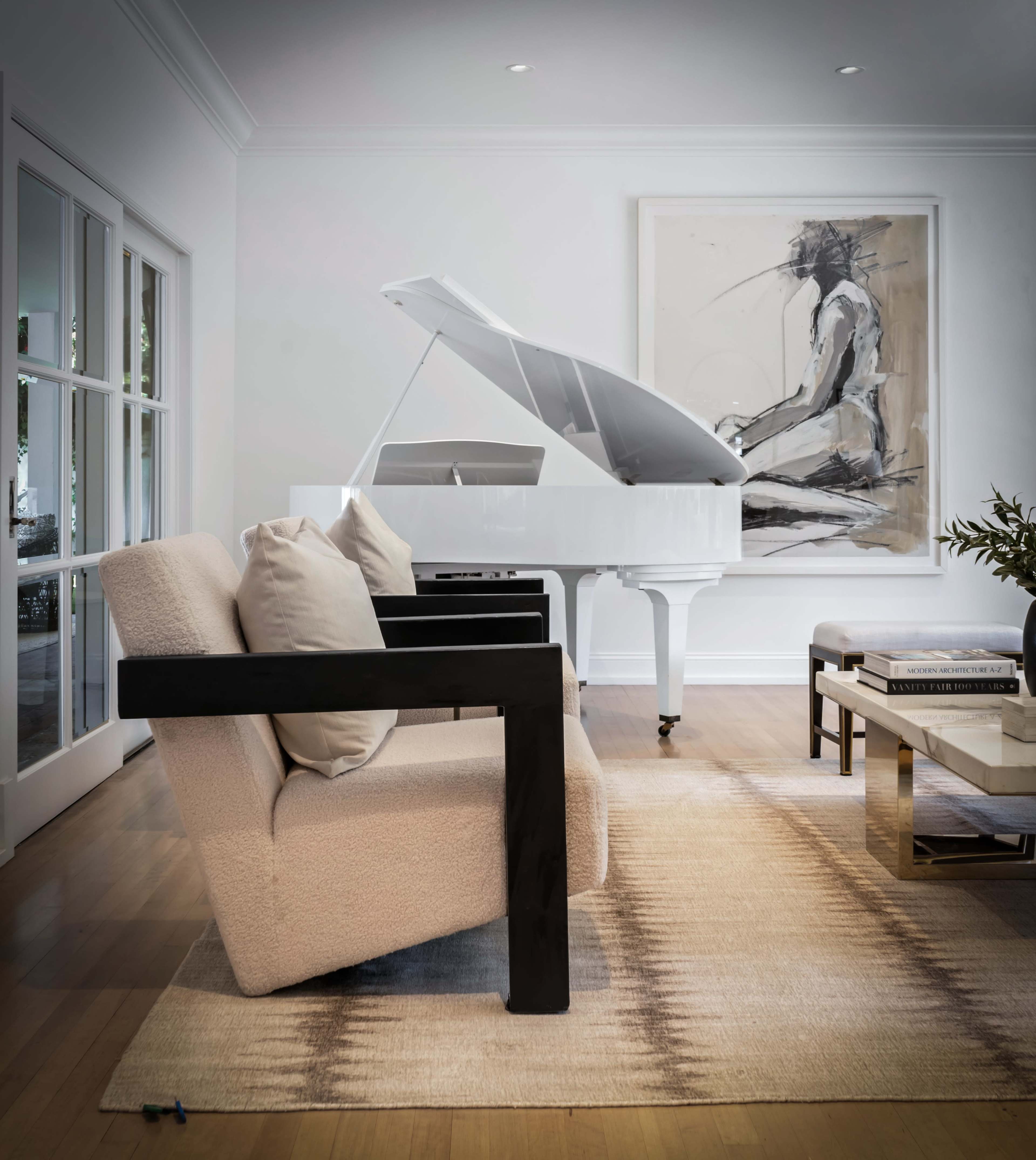 A white grand piano is positioned beside two modern armchairs in a brightly lit living room decorated with a large artwork and a coffee table.