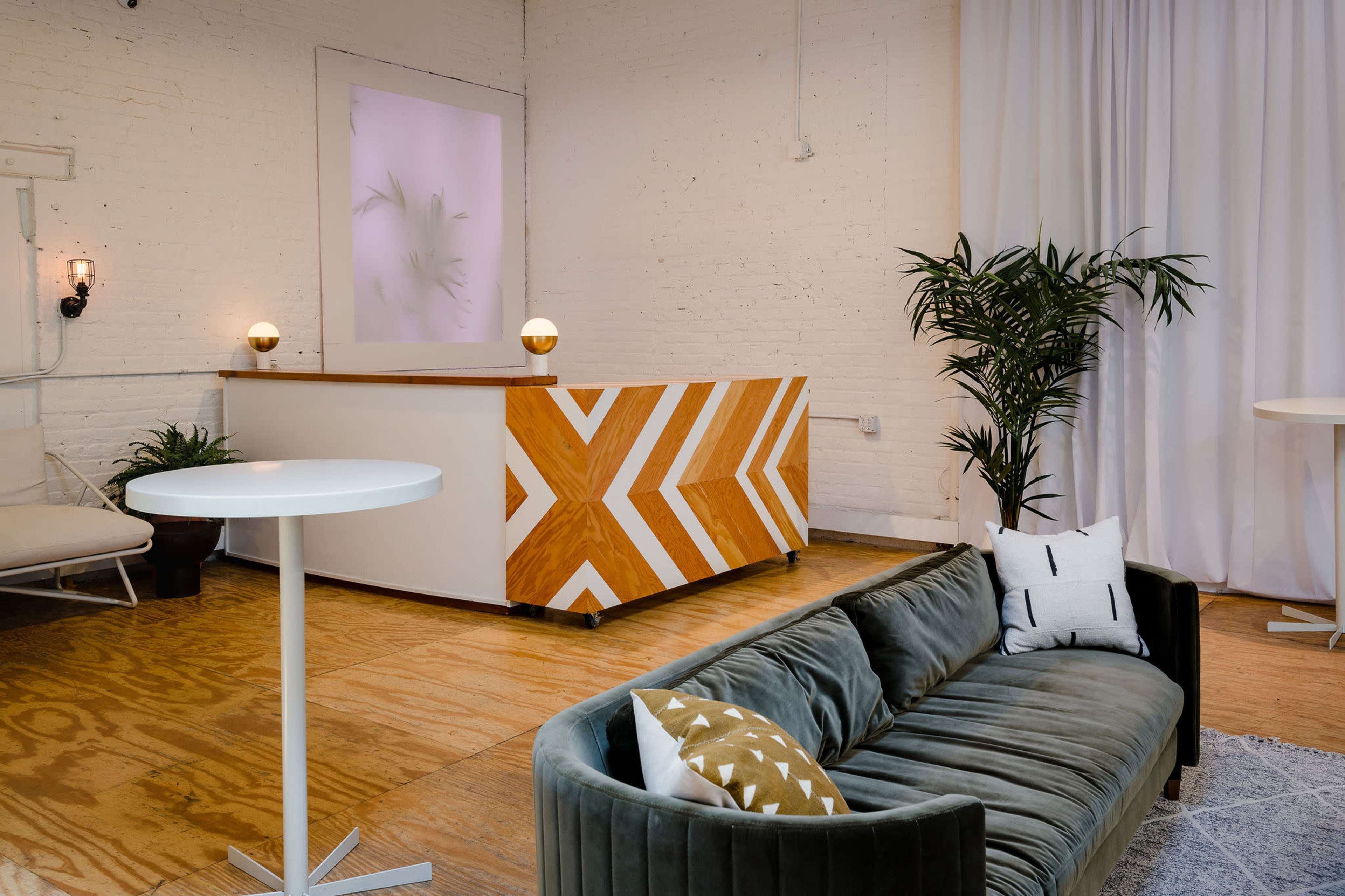 A modern reception area features a white and wood-striped front desk, a green curved sofa, and a potted plant against a white brick wall.