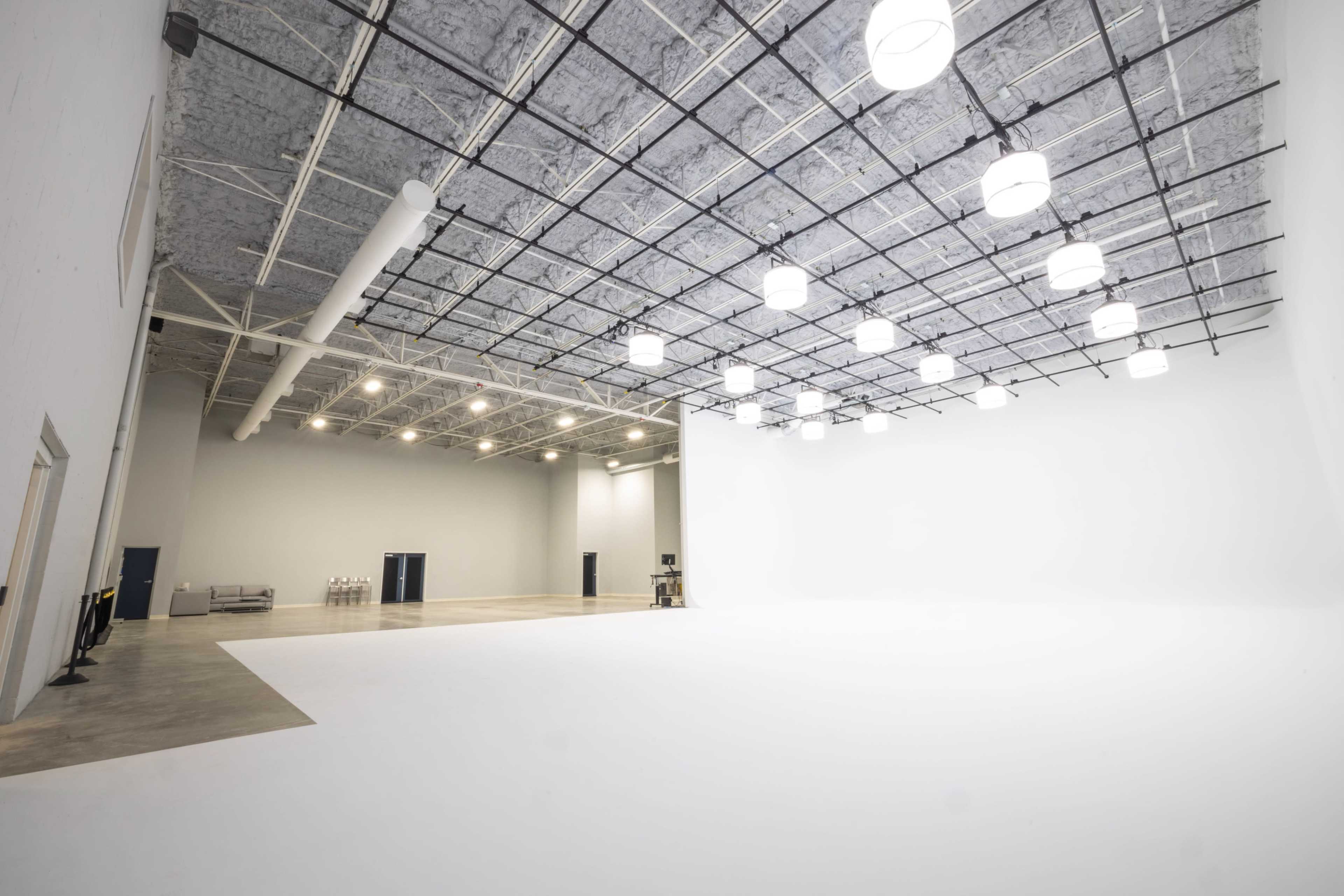 A large, empty studio space with a white wall and a ceiling grid of lights.