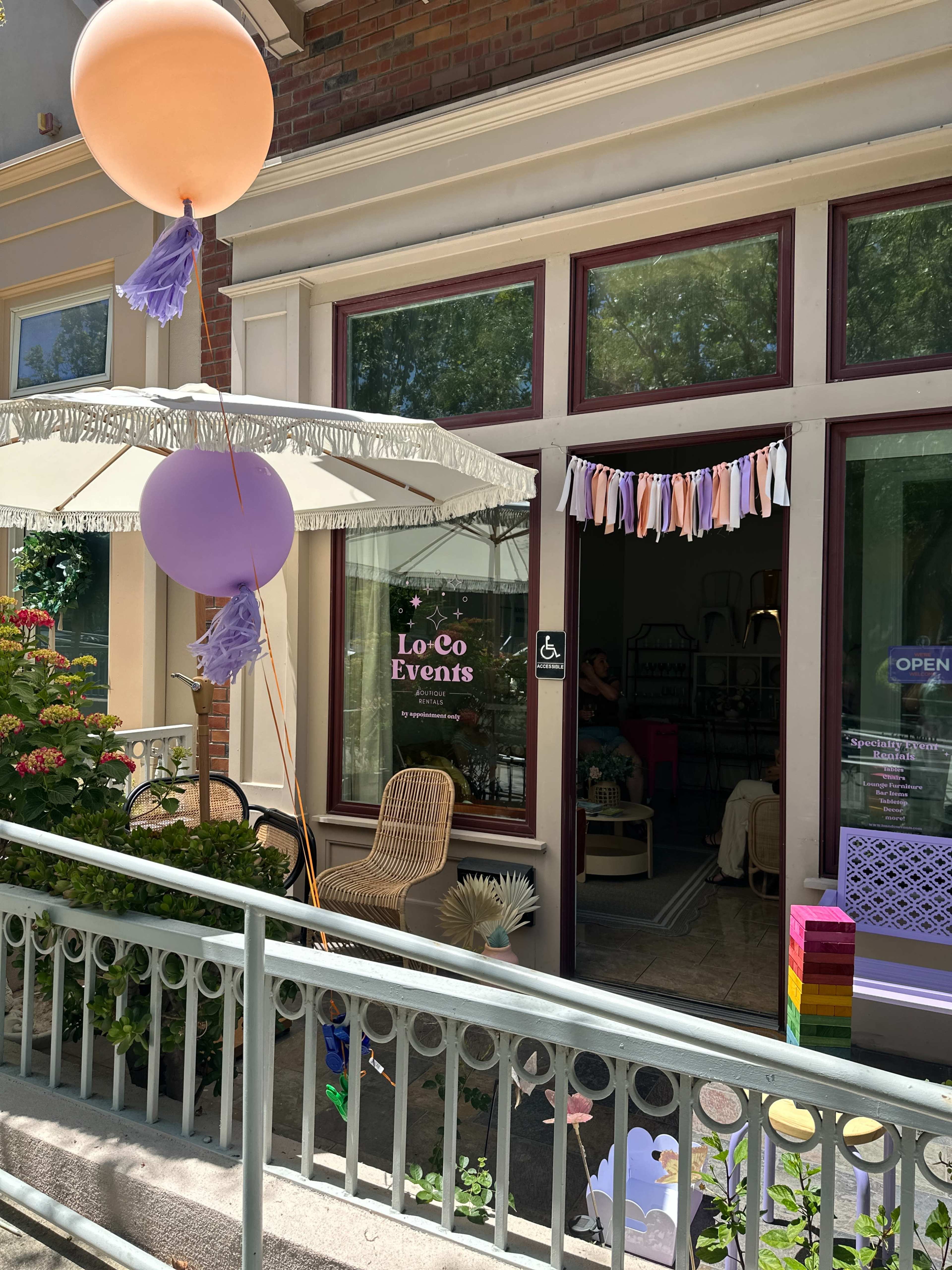 The image shows the entrance of "LoCo Events," featuring decorative balloons, a shaded patio area, and colorful garlands hanging across the doorway.