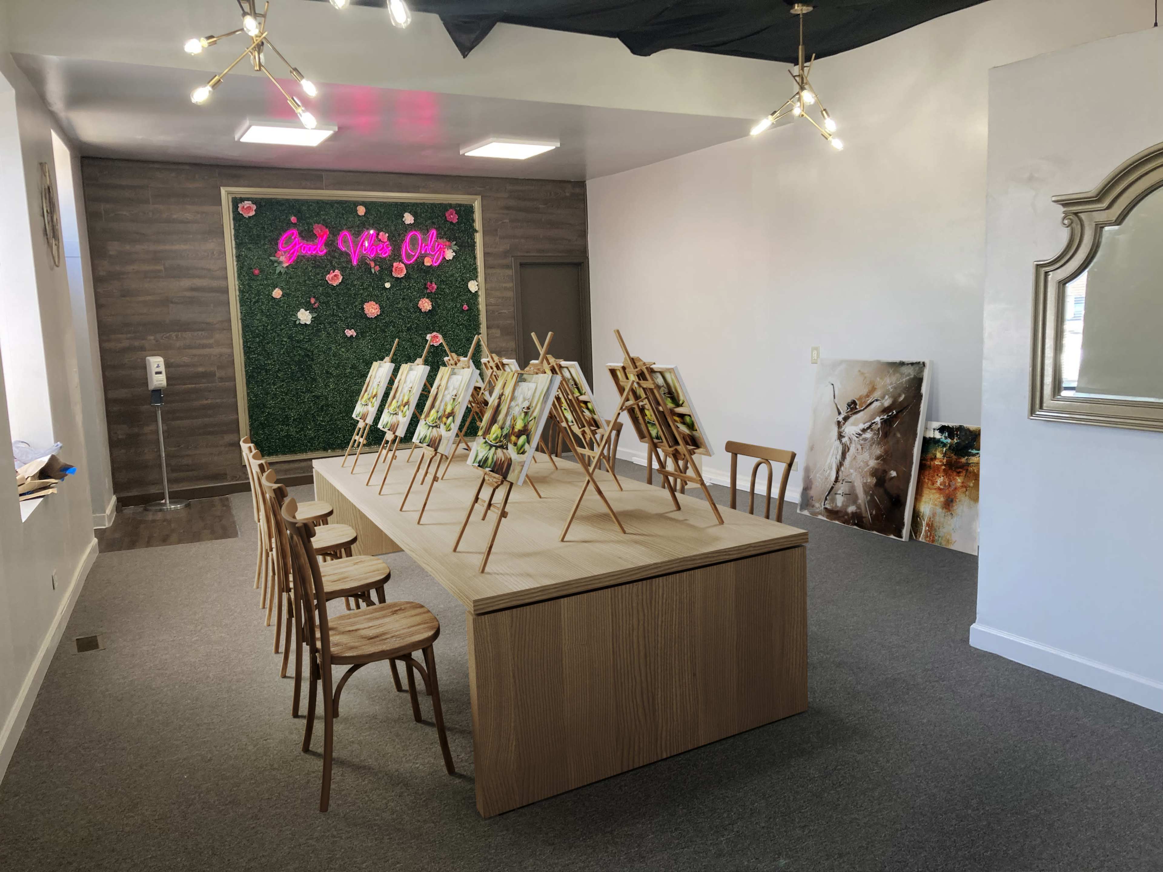 A spacious art studio with a large wooden table set for painting, surrounded by several easels displaying canvases and adorned with decorative elements on the walls.