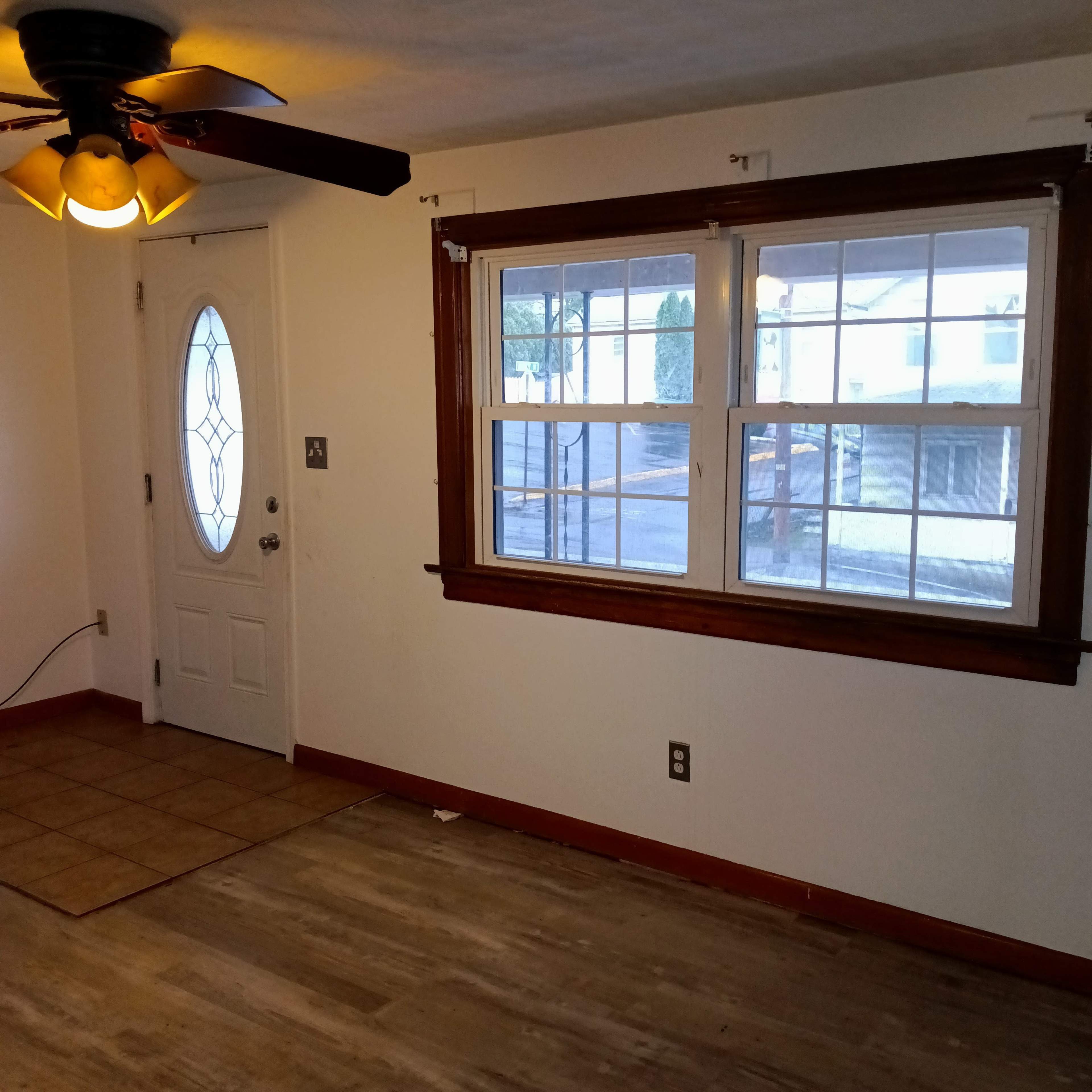 A room features a door with a decorative window, a ceiling fan, and large windows with wooden trim.