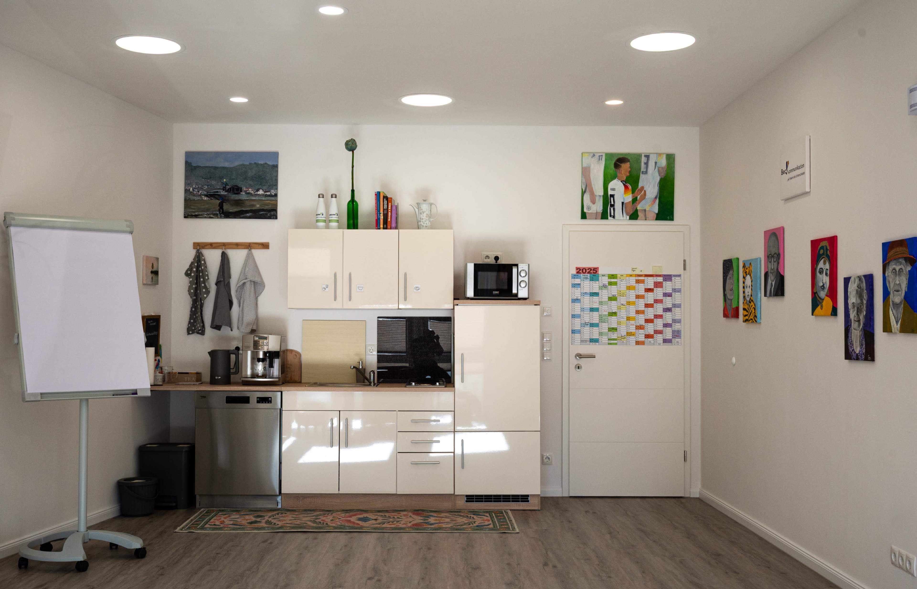 The image shows a modern kitchen area with a refrigerator, microwave, and various artworks on the walls.
