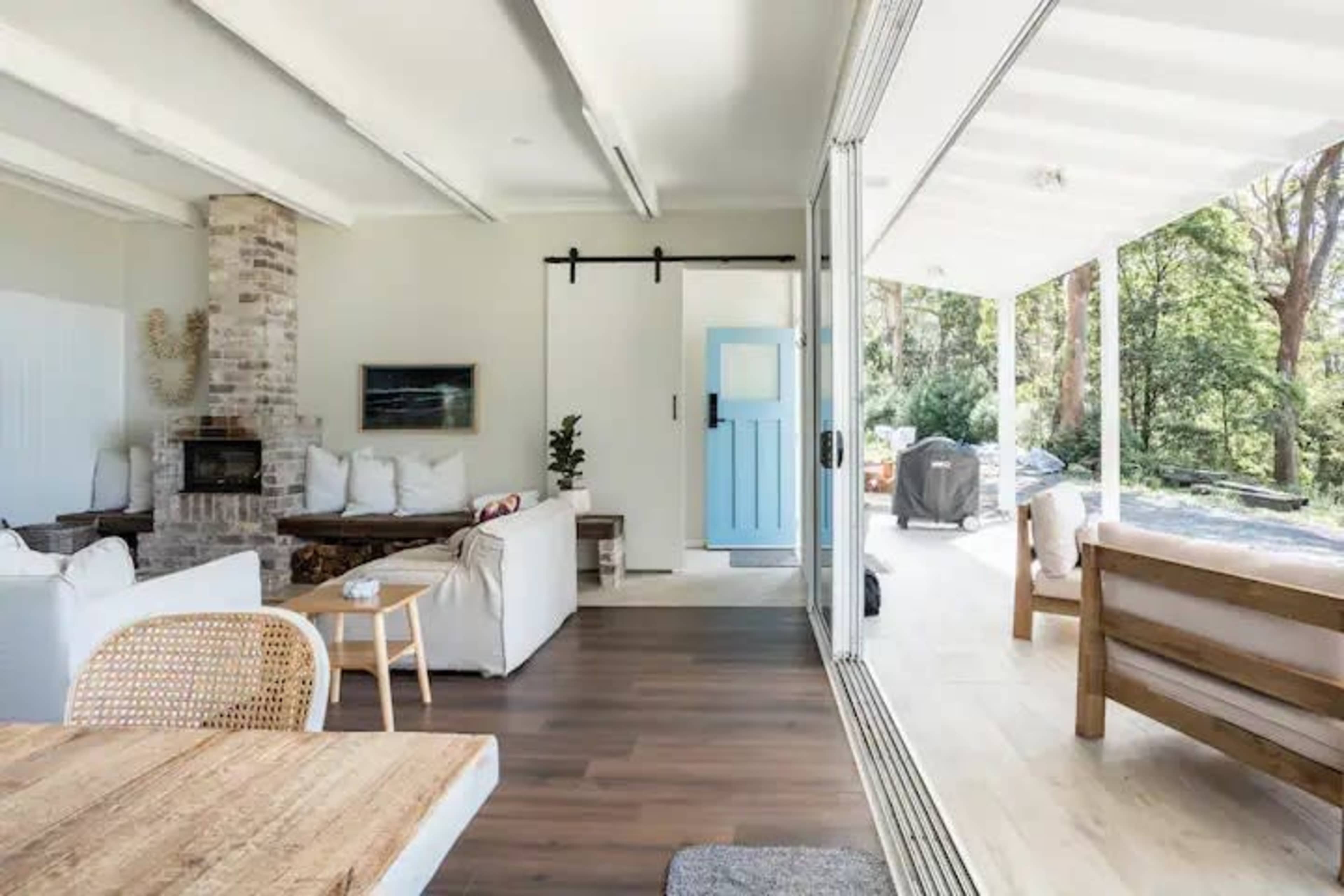 A modern living space with a fireplace, a white sofa, and a blue door leading to an outdoor area surrounded by trees.