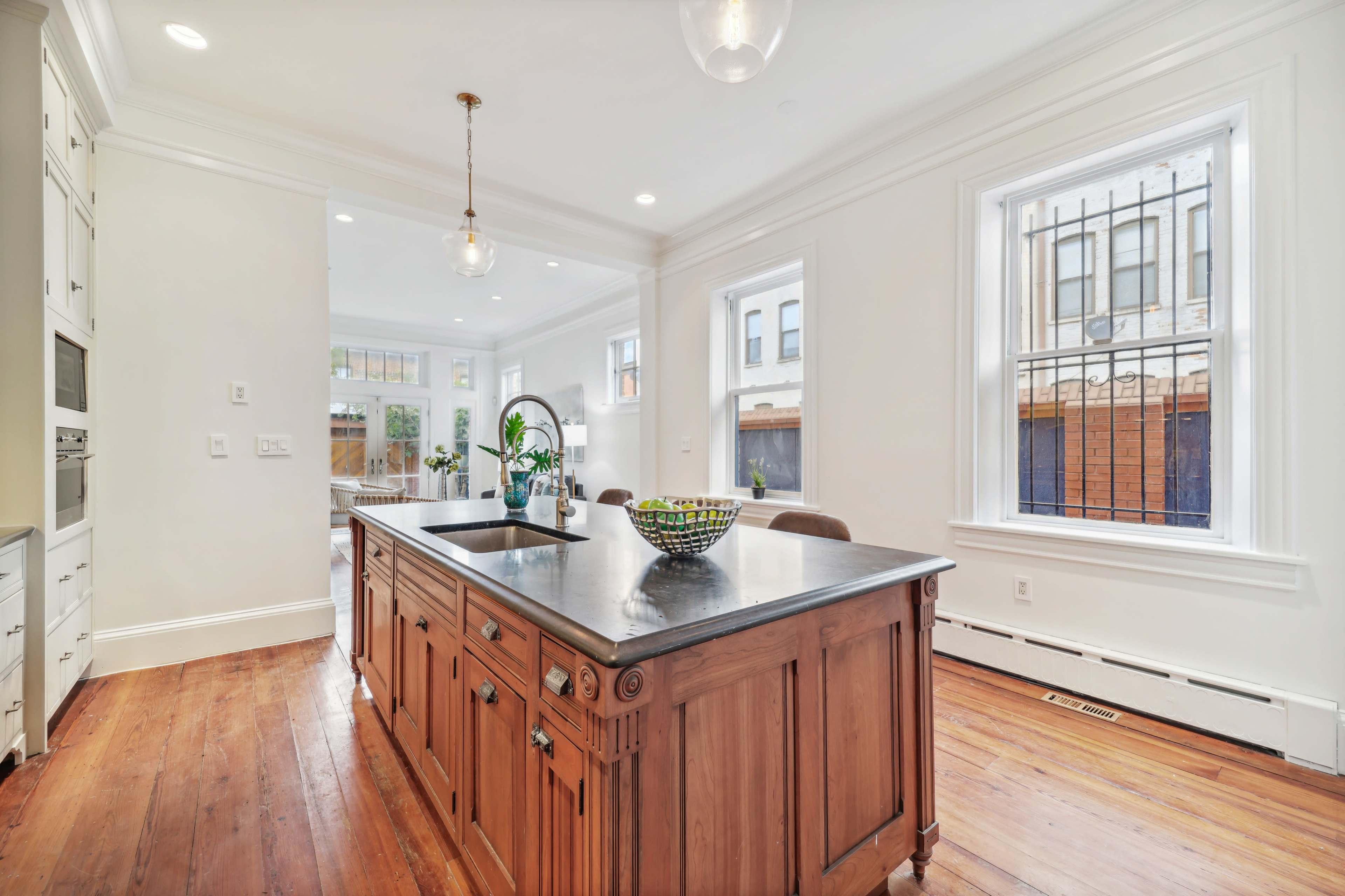 A spacious kitchen features a central wooden island with a black countertop and large windows allowing natural light to fill the room.