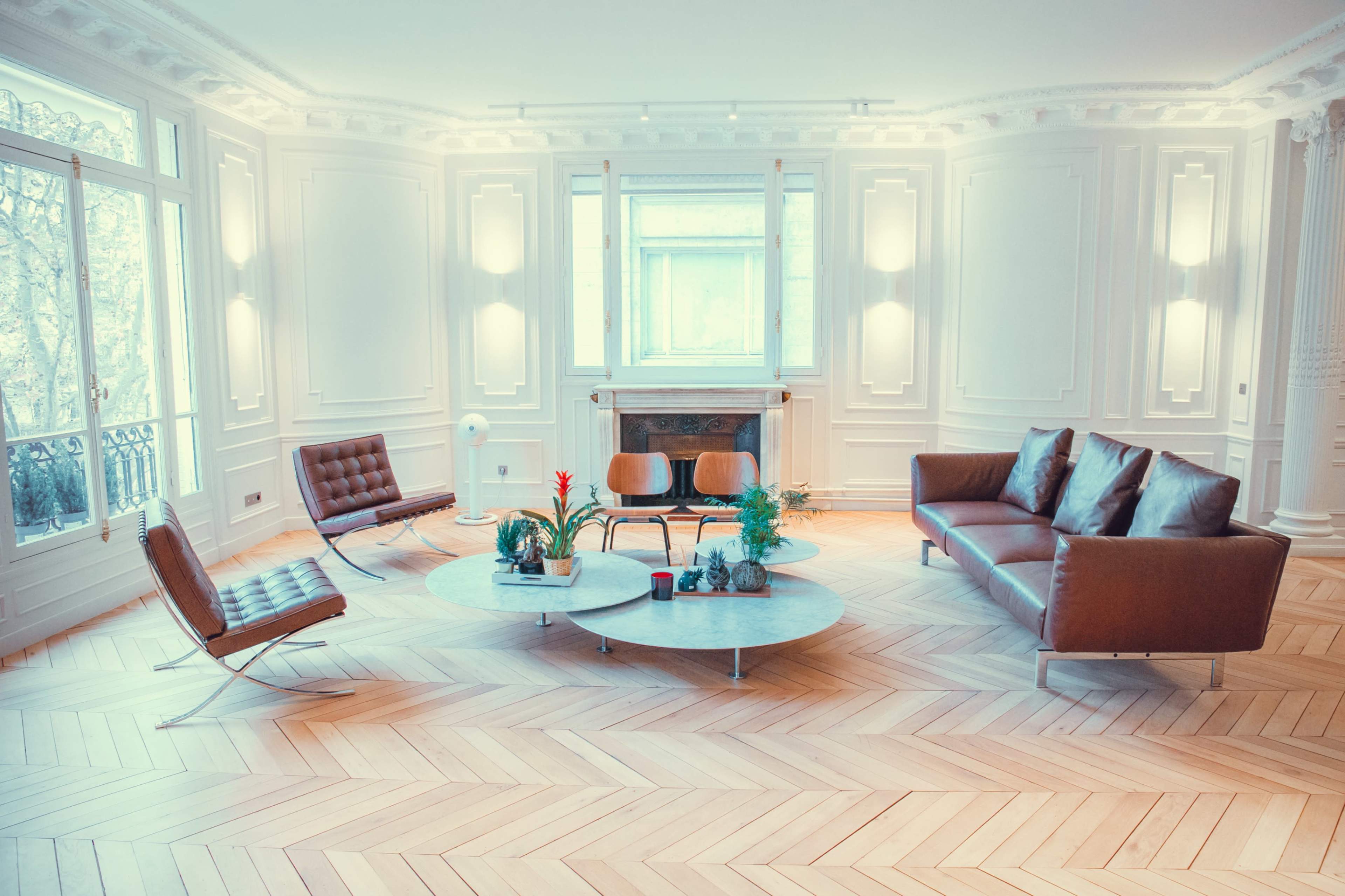 The image depicts a spacious and elegantly furnished living room with two sofas, a coffee table, and wooden herringbone flooring.