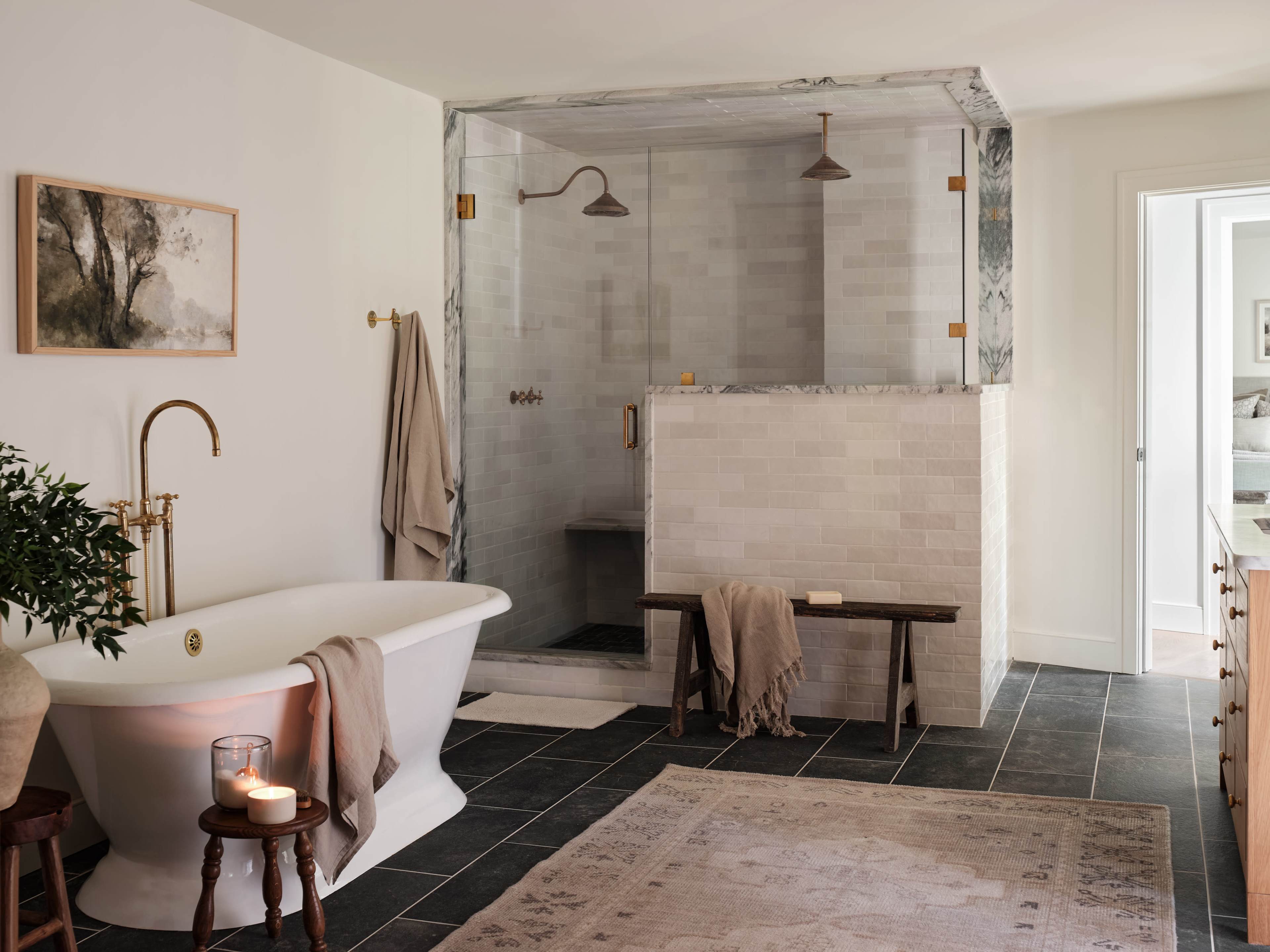 A bathroom features a freestanding bathtub, a walk-in shower with a glass enclosure, and a wooden bench, all set against a backdrop of neutral-toned tiles and decor.