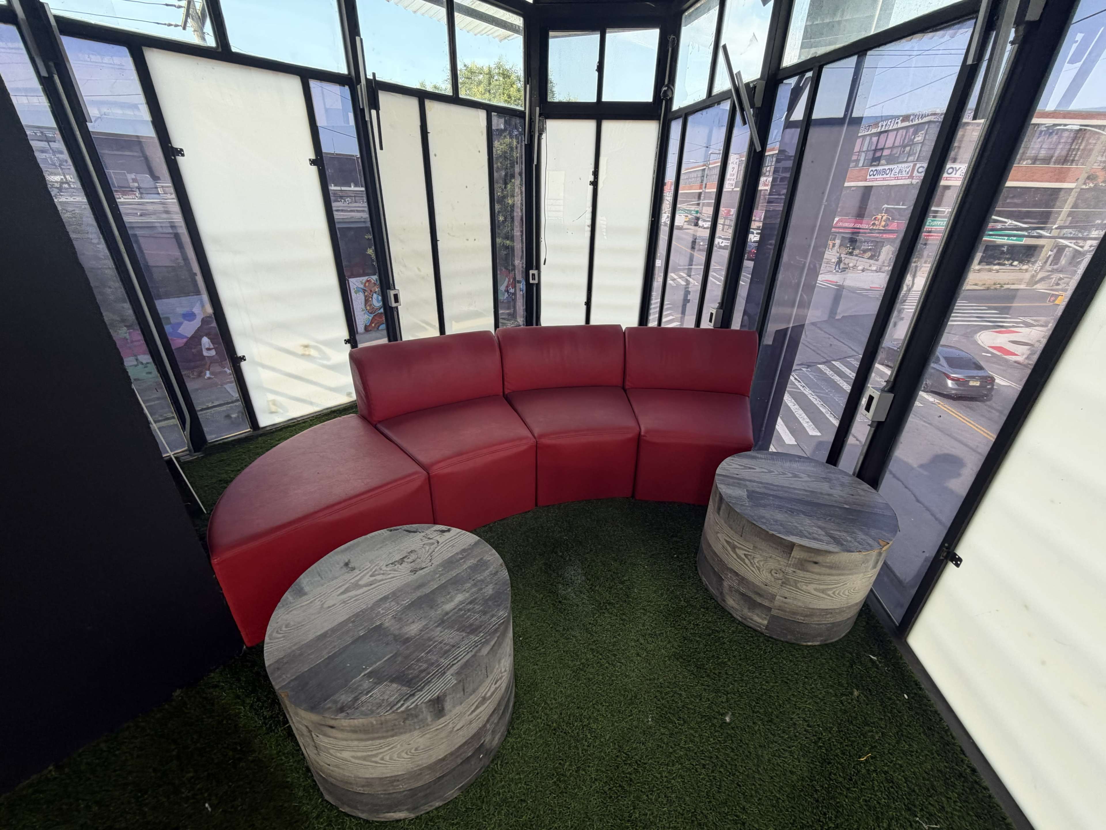 The image shows a curved red seating arrangement with two gray wooden tables in a glass-enclosed space.