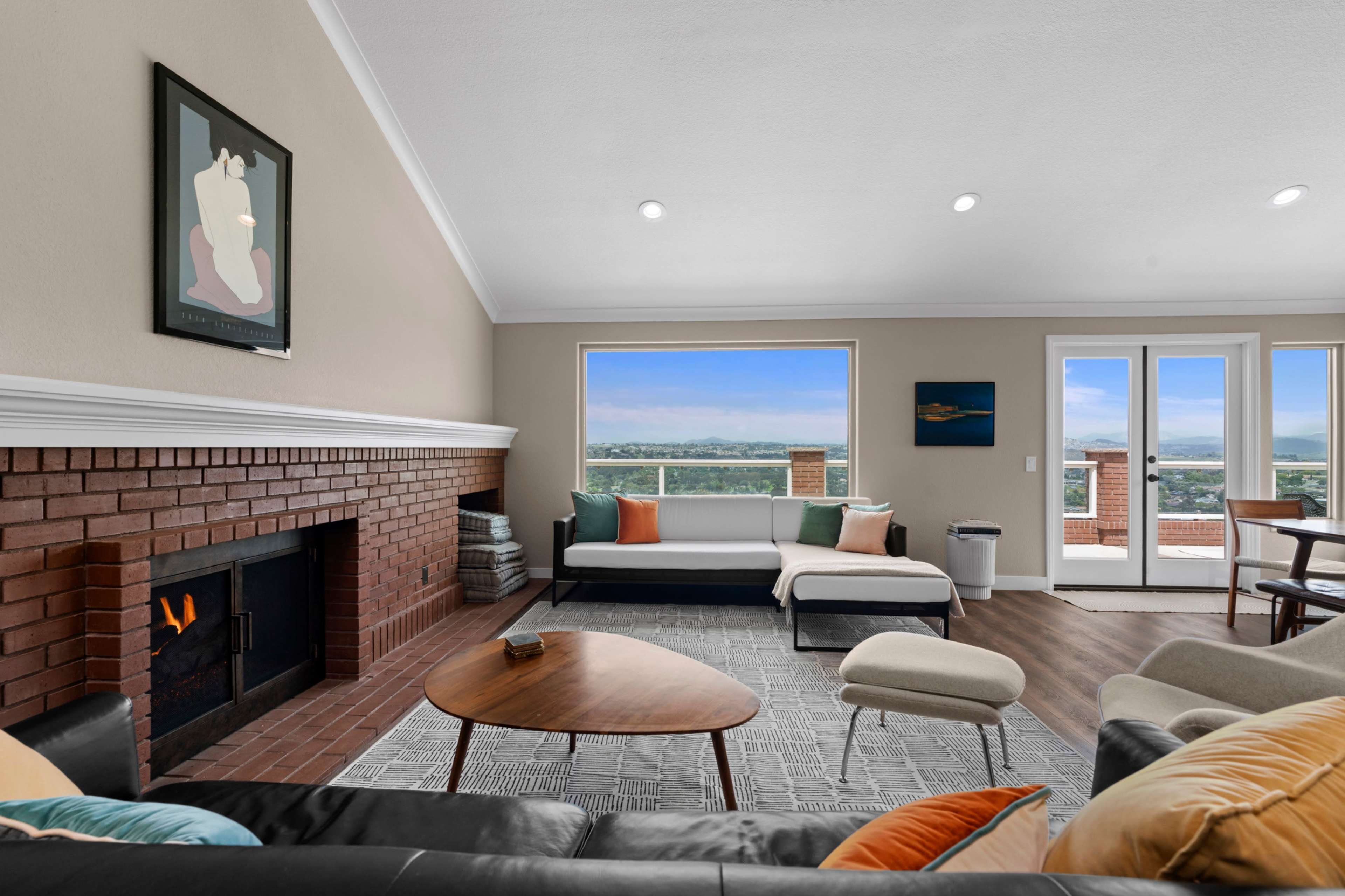The living room features a modern design with a fireplace, large windows showcasing a panoramic view, and a mix of comfortable seating options.